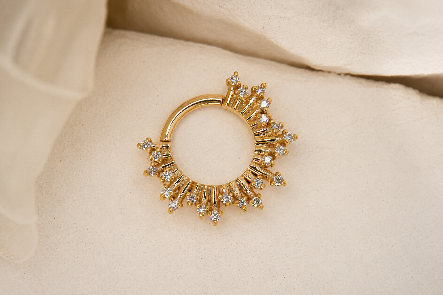 Gold hoop earring with small diamonds, resting on a beige fabric background.