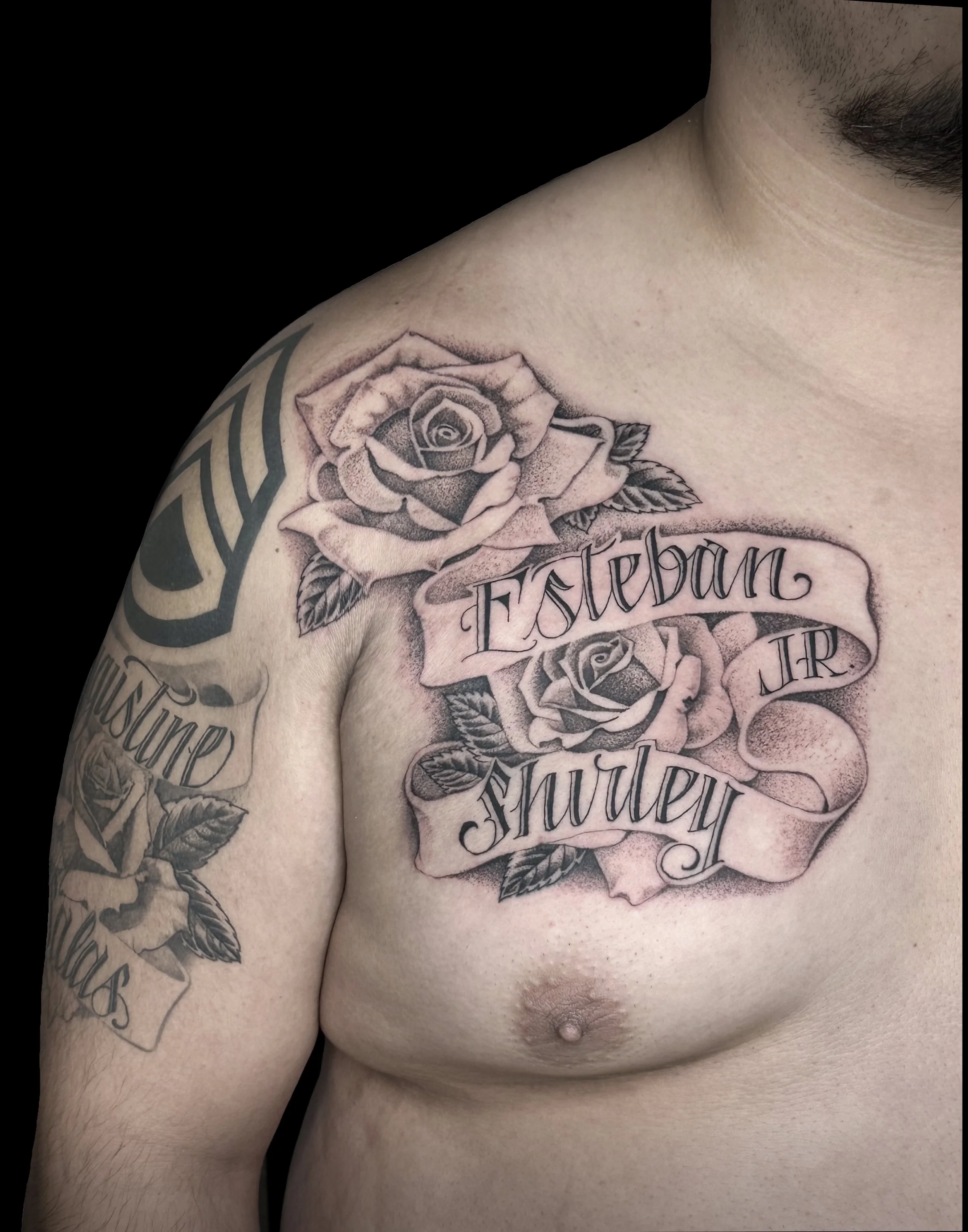 Close-up of a person's upper chest and shoulder with a large tattoo of roses and cursive writing.