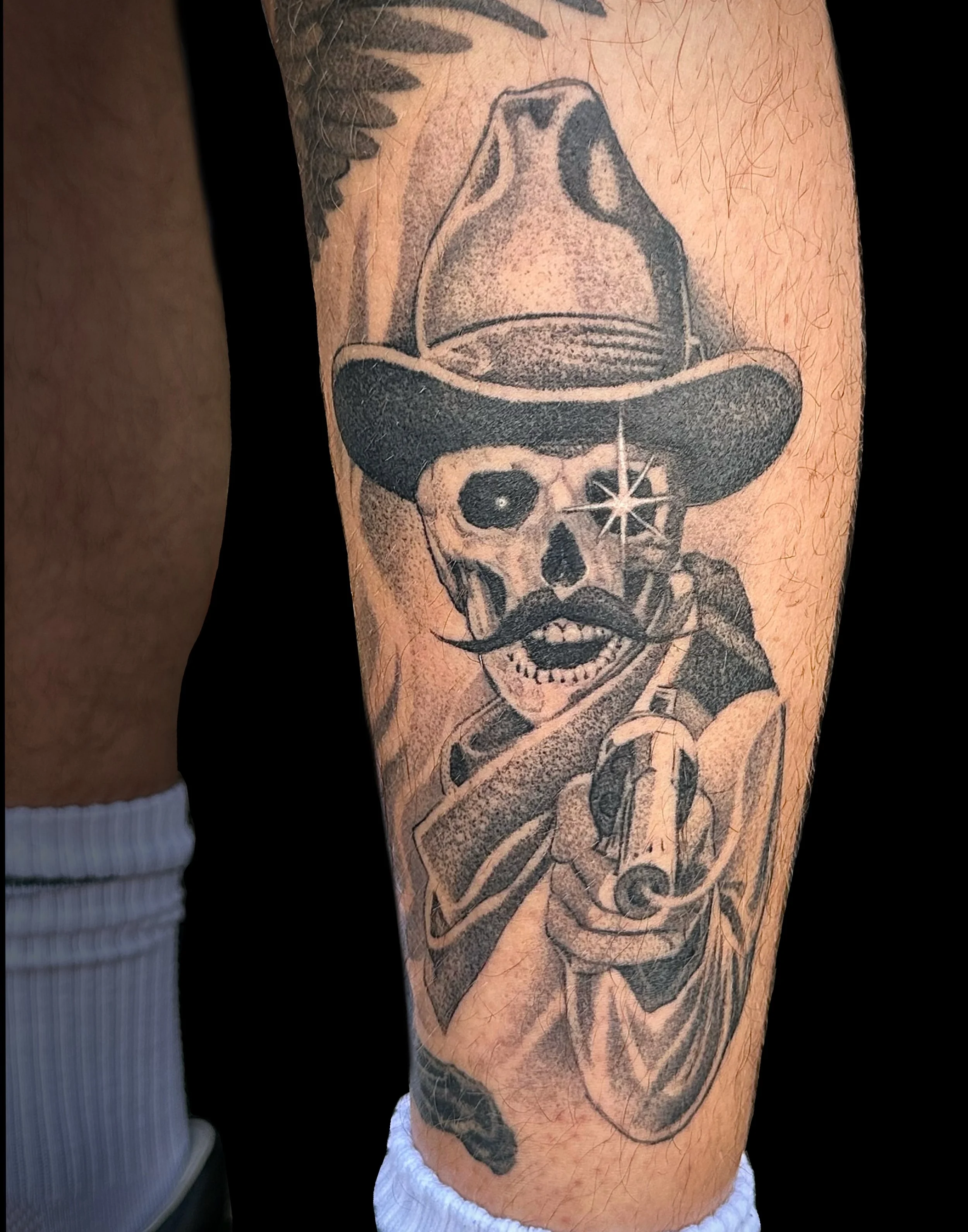 Tattoo of a skeleton wearing a cowboy hat and a mustache on a person's arm.