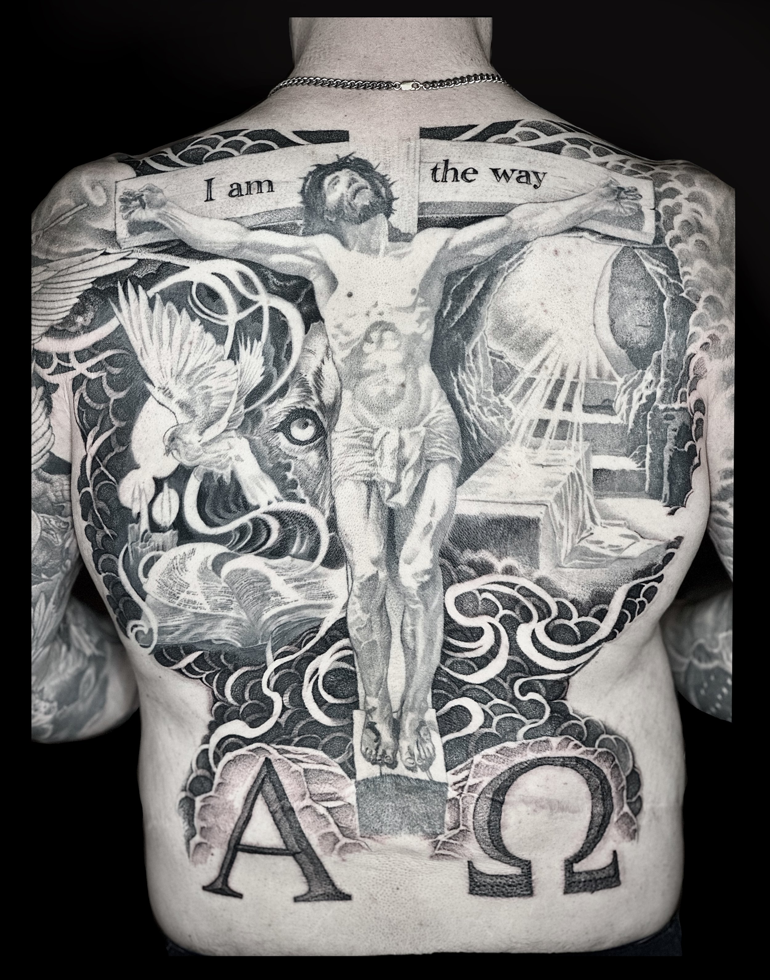 Black and gray tattoo on a person's back depicting Jesus Christ on the cross, with the words "I am the way" above.