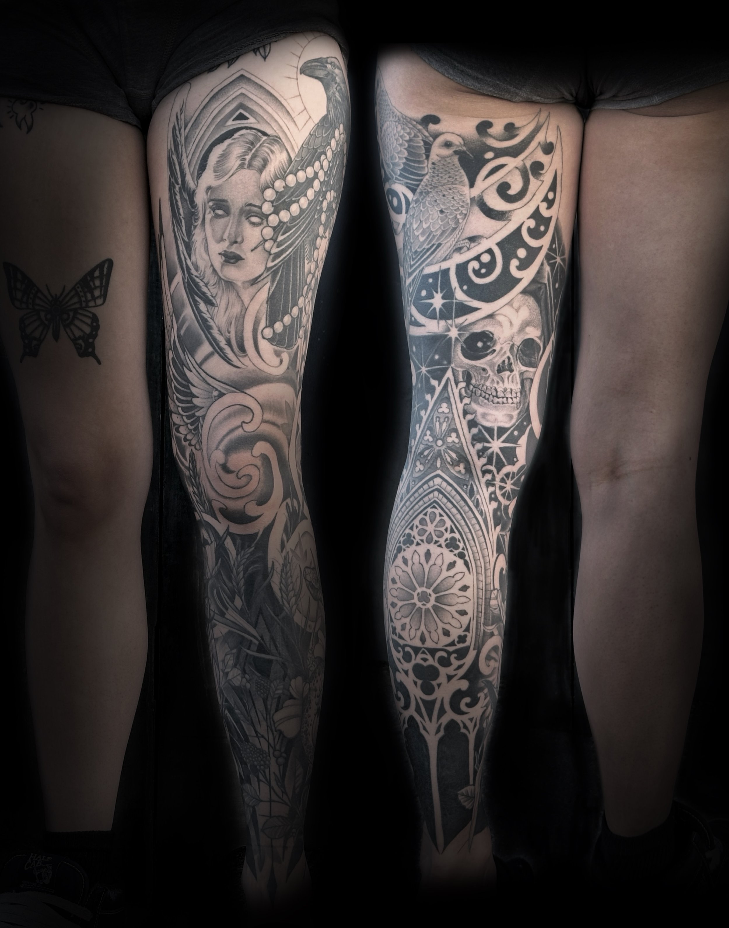 Close-up of two tattooed legs with detailed black and gray tattoos, including a woman with long flowing hair and a bird with outstretched wings, along with skulls and intricate patterns.