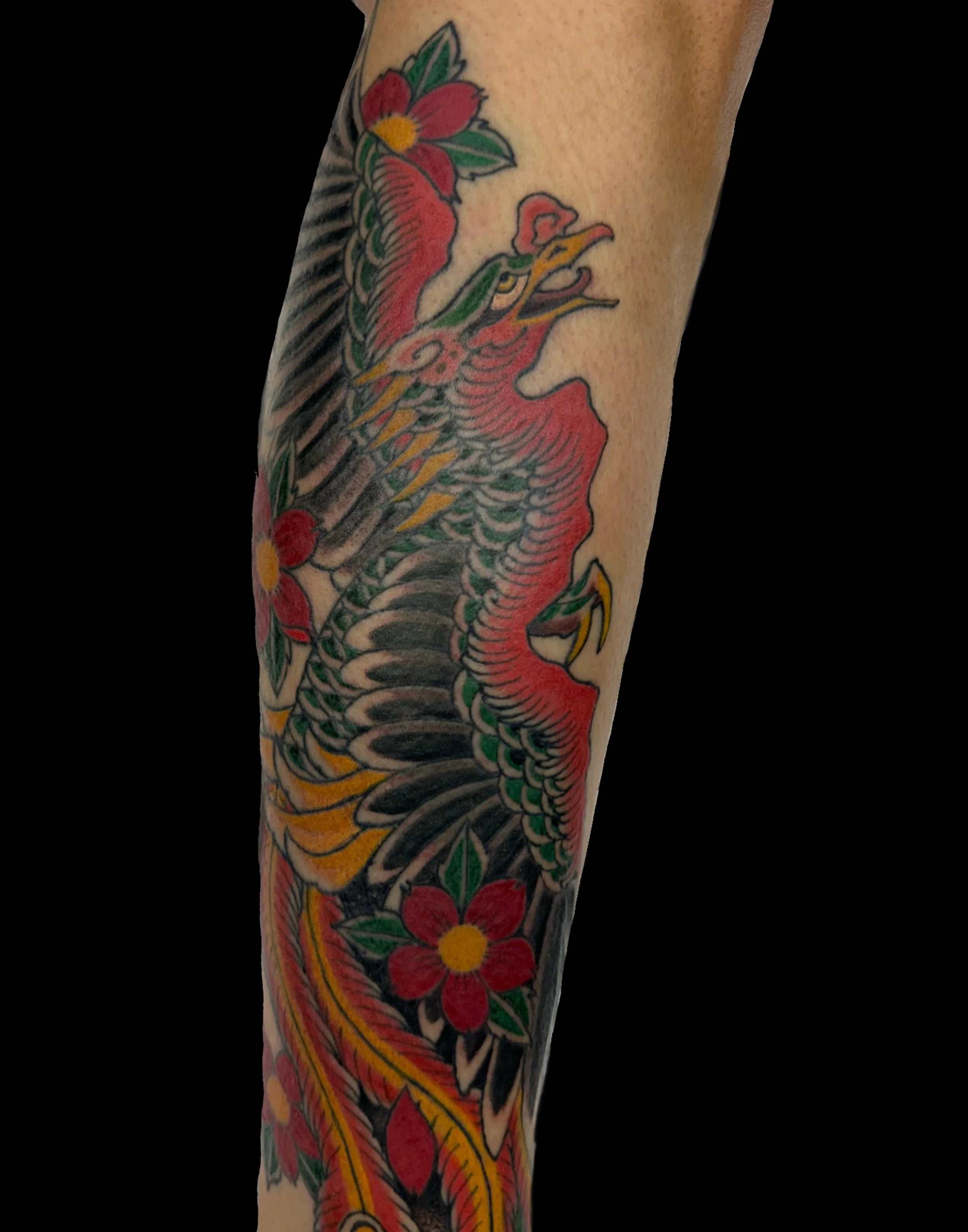 Tattoo of a dragon with red, green, yellow, and black colors on a person's arm.