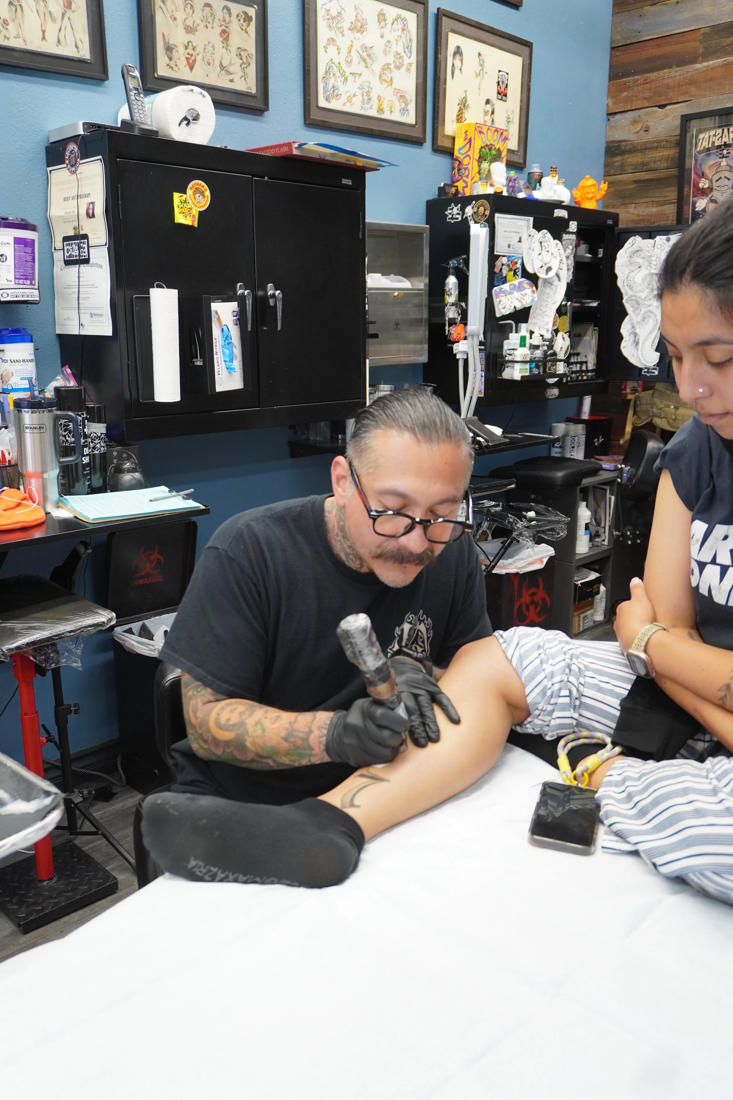 Tattoo artist tattooing a person's arm in tattoo studio with tattoo designs on the wall
