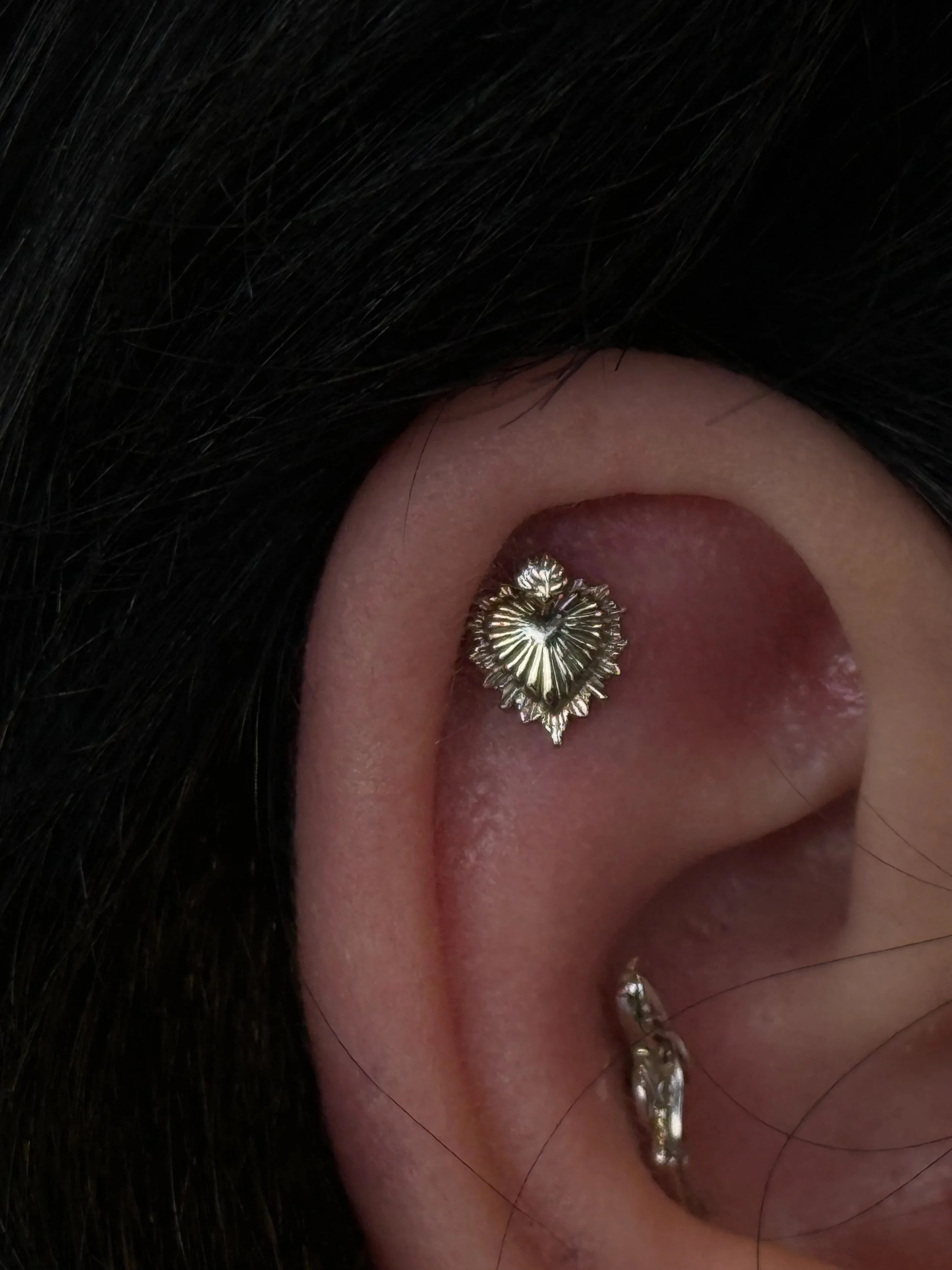 Close-up of a person's ear adorned with multiple gold earrings, with black hair partially covering the ear.