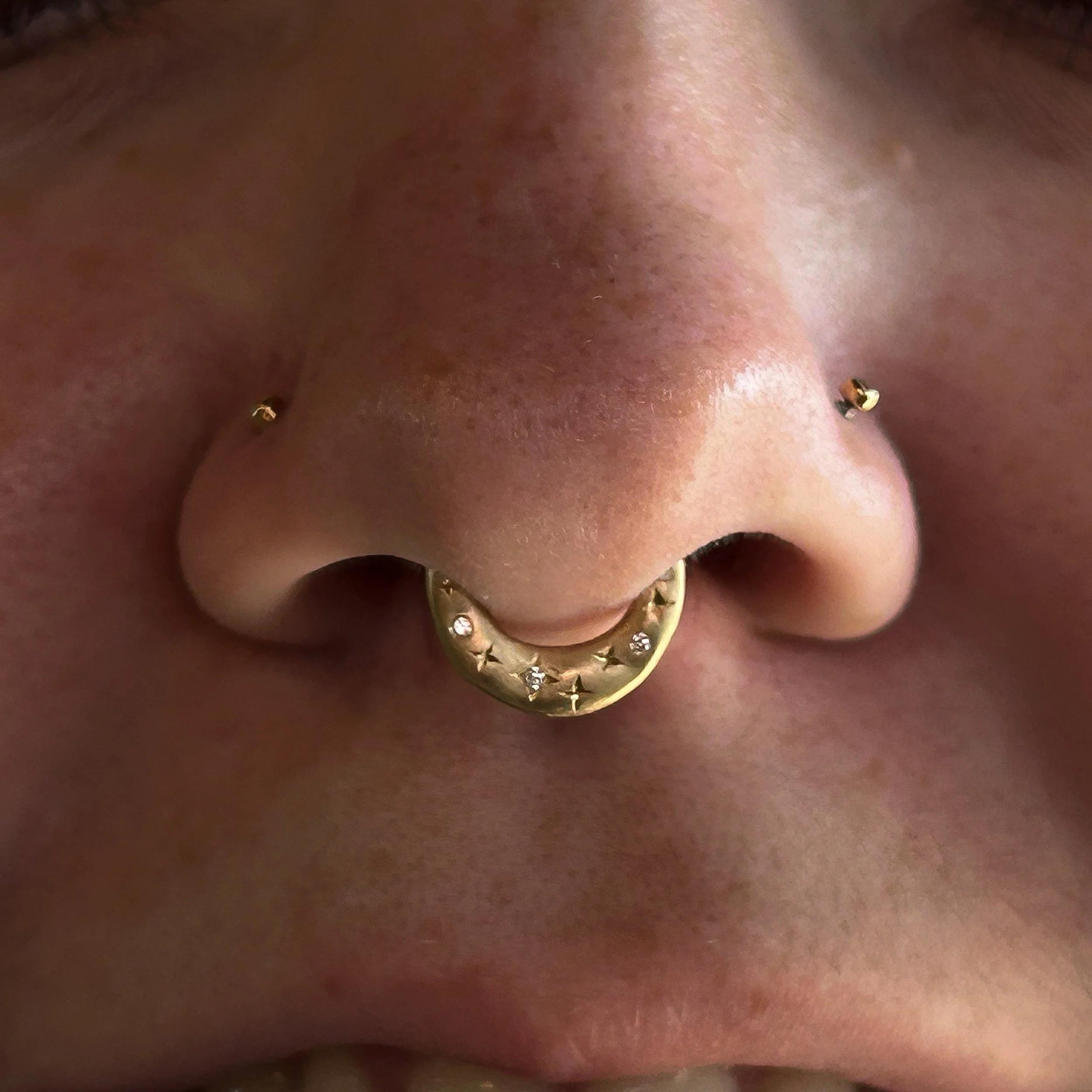 Close-up of a pierced human nose with a gold septum ring adorned with small gemstones.