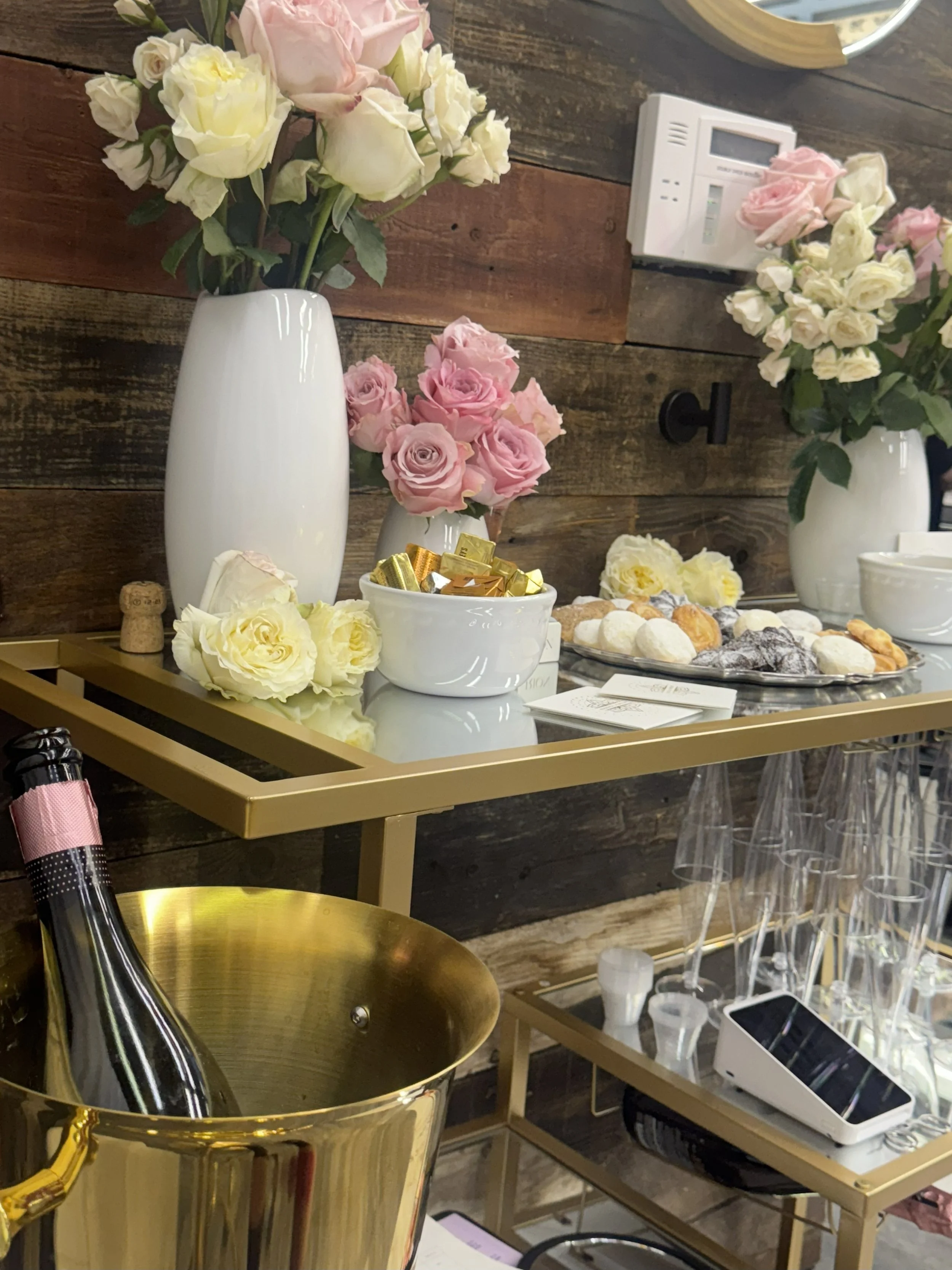 A display of floral arrangements in vases, along with trays of assorted cookies and snacks on a table at an event or gathering.