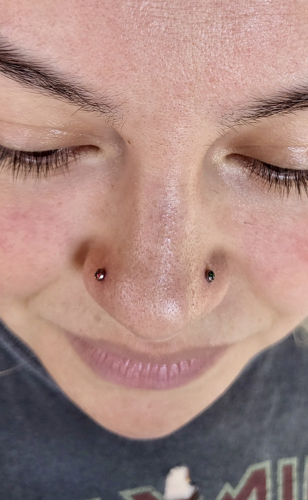 Close-up of a person's face with closed eyes, a nose piercing, and light skin with freckles.
