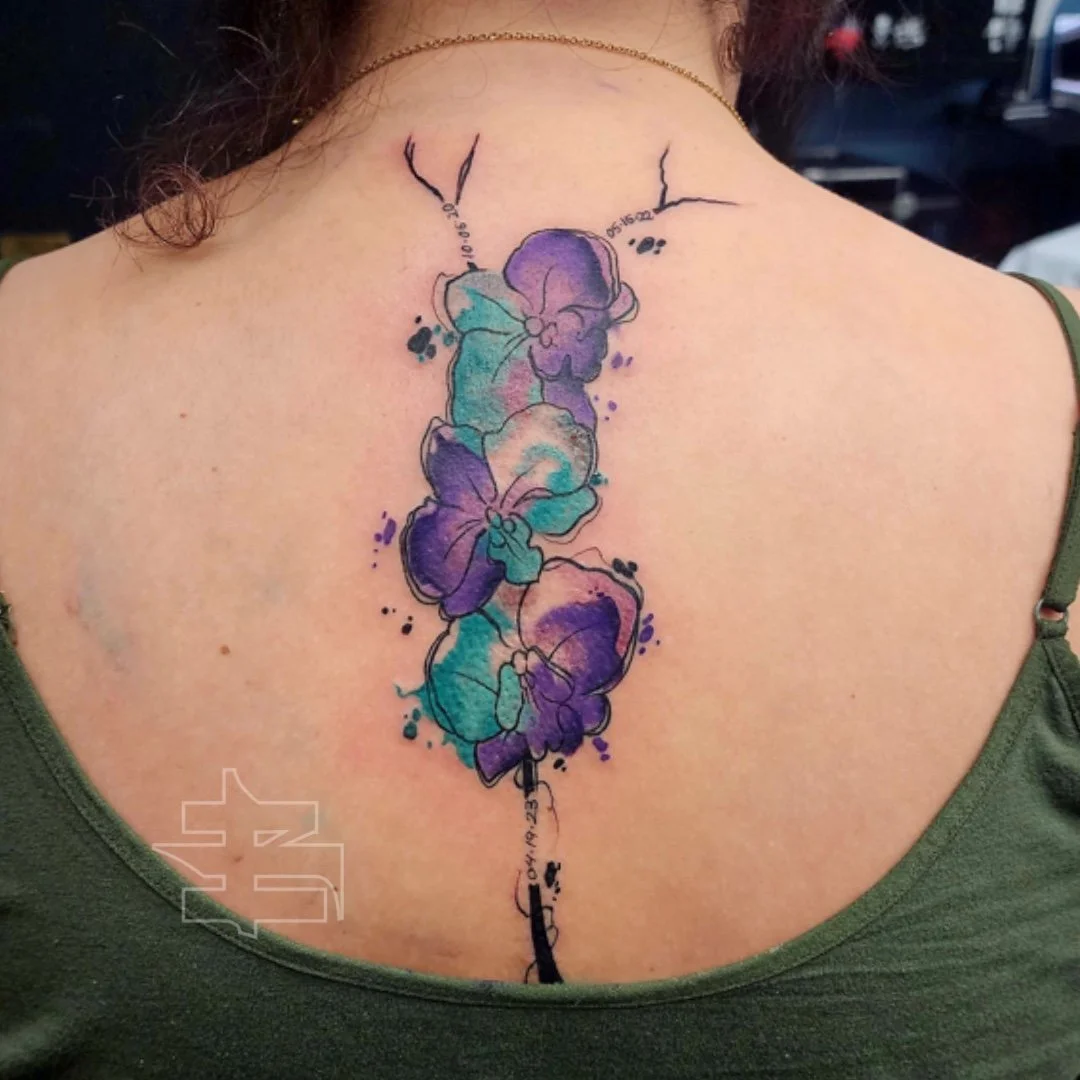 Watercolor tattoo of purple and turquoise flowers on a person's back.
