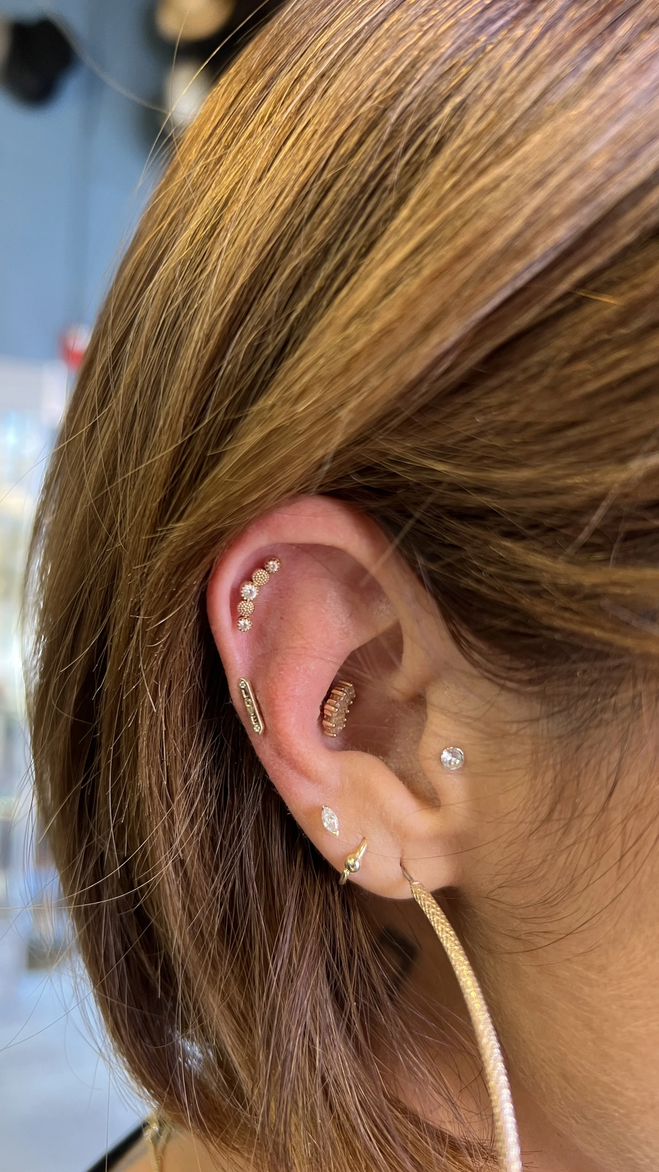 Close-up of a person's ear with multiple gold and diamond earrings, including hoops, studs, and a bar.