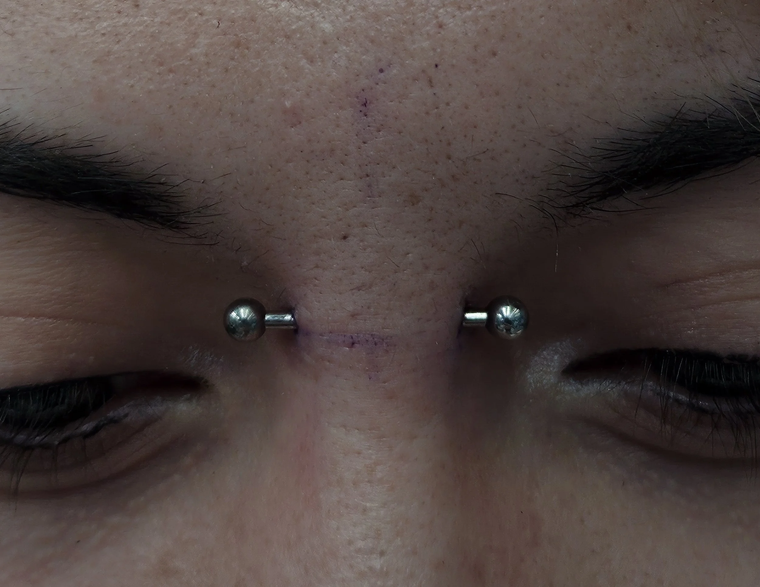 Close-up of a person's face with a septum piercing and a small tattoo above the eyebrow
