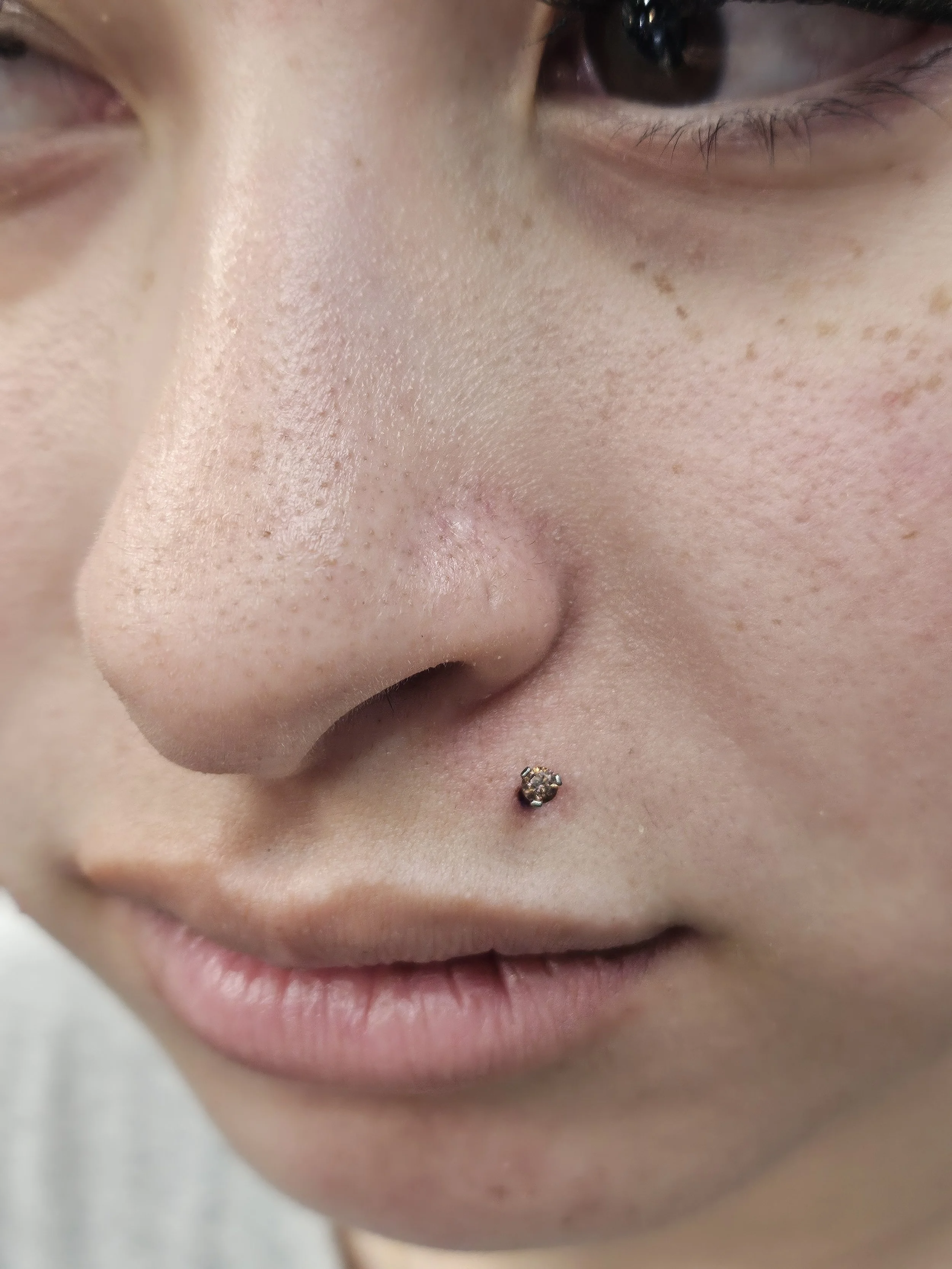 Close-up of a person's nose, lips, and part of the face, with a septum piercing featuring a small, shiny jewelry piece.