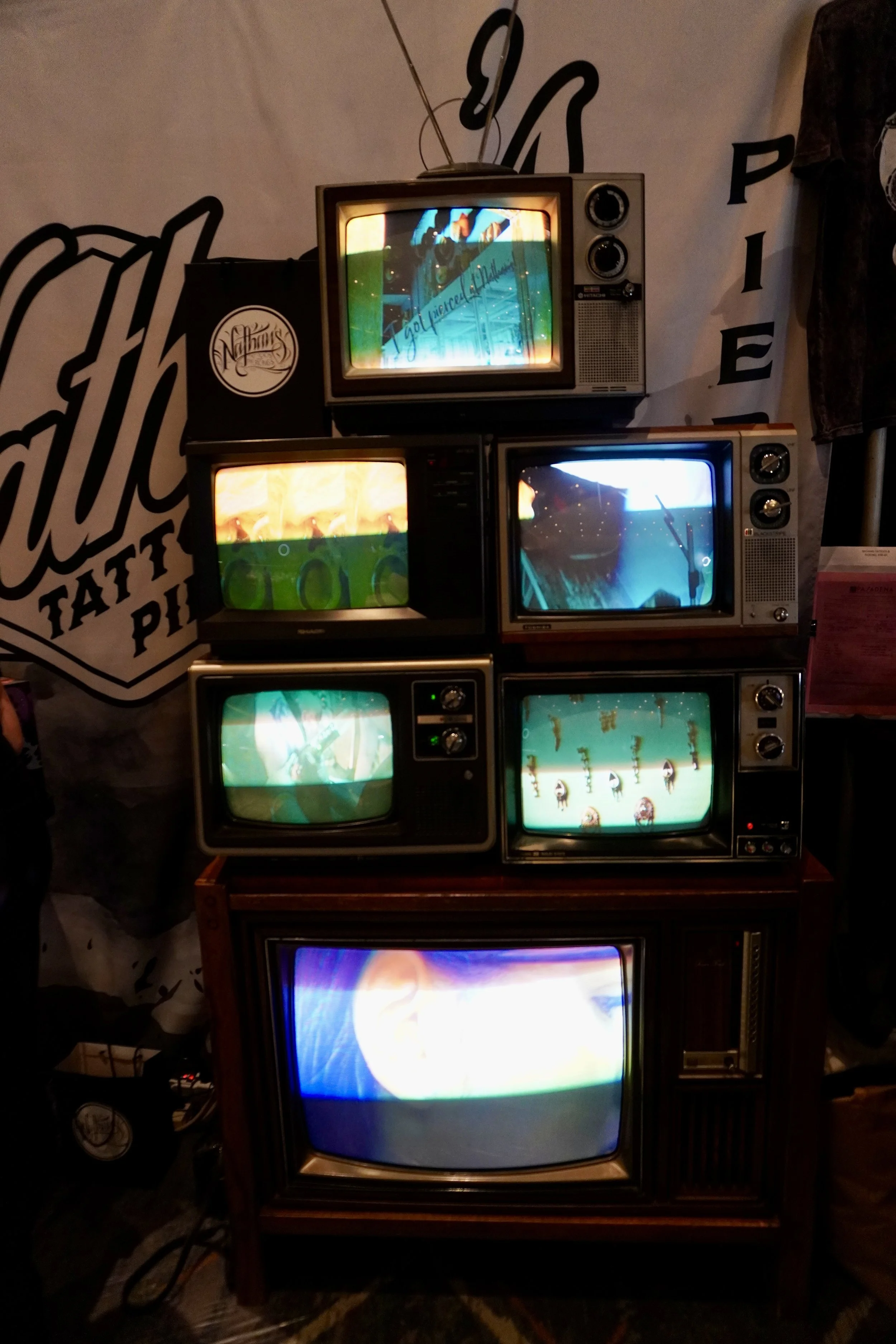 A collection of vintage CRT televisions stacked on a wooden table, all displaying colorful, distorted images and video game graphics.