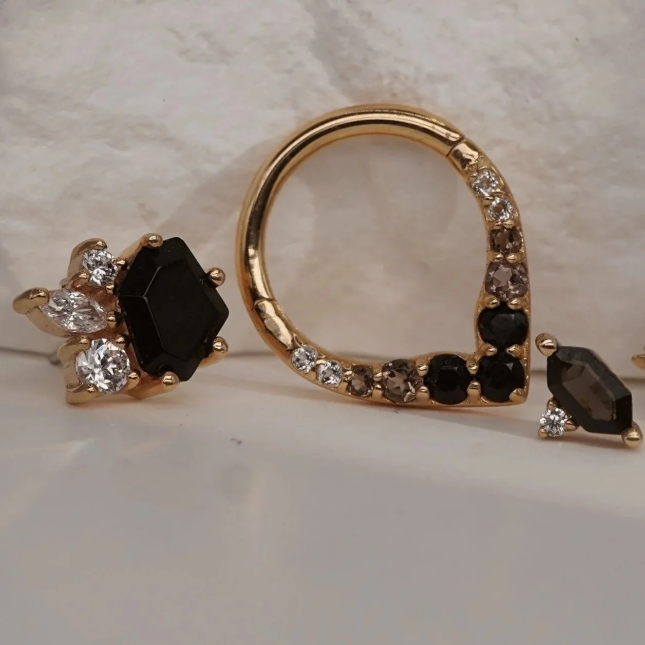 A gold ring with black and clear gemstones, a black and clear gemstone ring, and a gold and black gemstone ring with multiple clear gemstones, displayed against a neutral background.