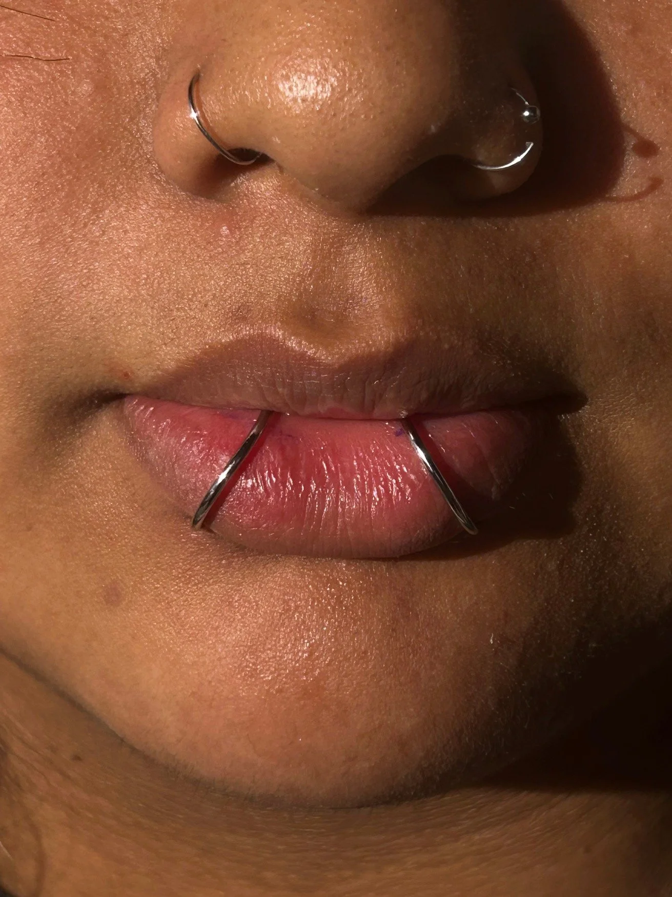 Close-up of a person's lips with a tongue piercing and a nose ring.