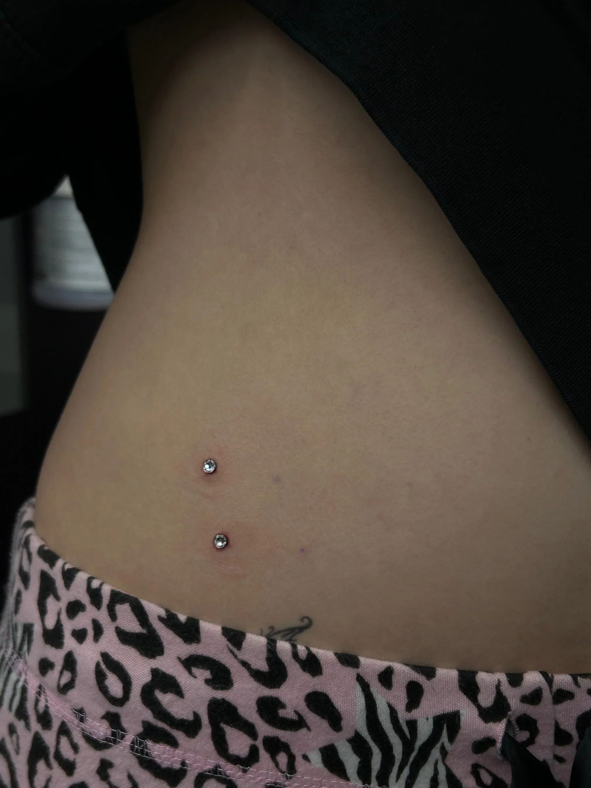Close-up of a person's abdomen with a belly button piercing, wearing leopard print clothing.