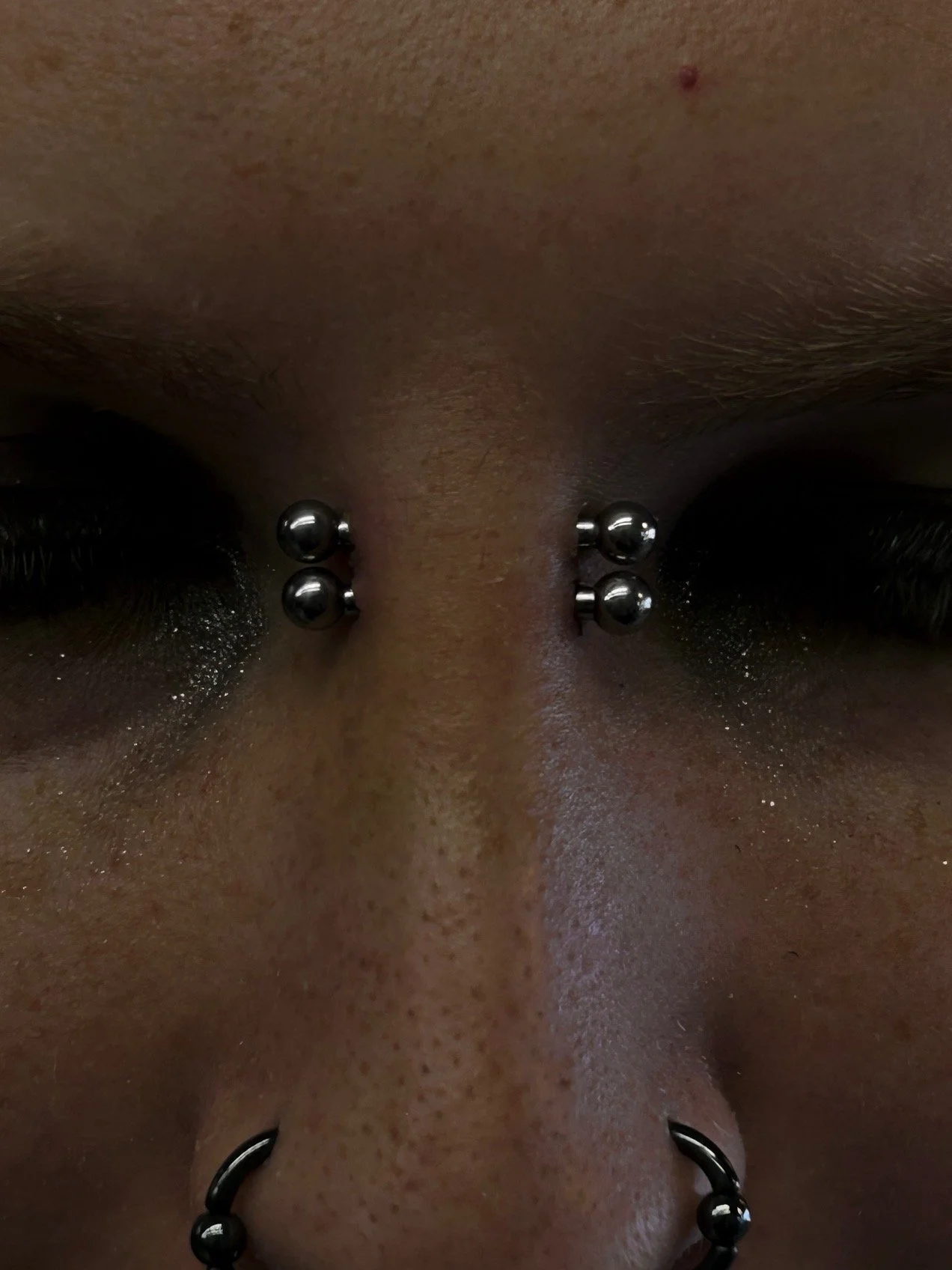 Close-up of a person's nose and upper lip with multiple metallic piercings in nostrils, septum, and upper lip.