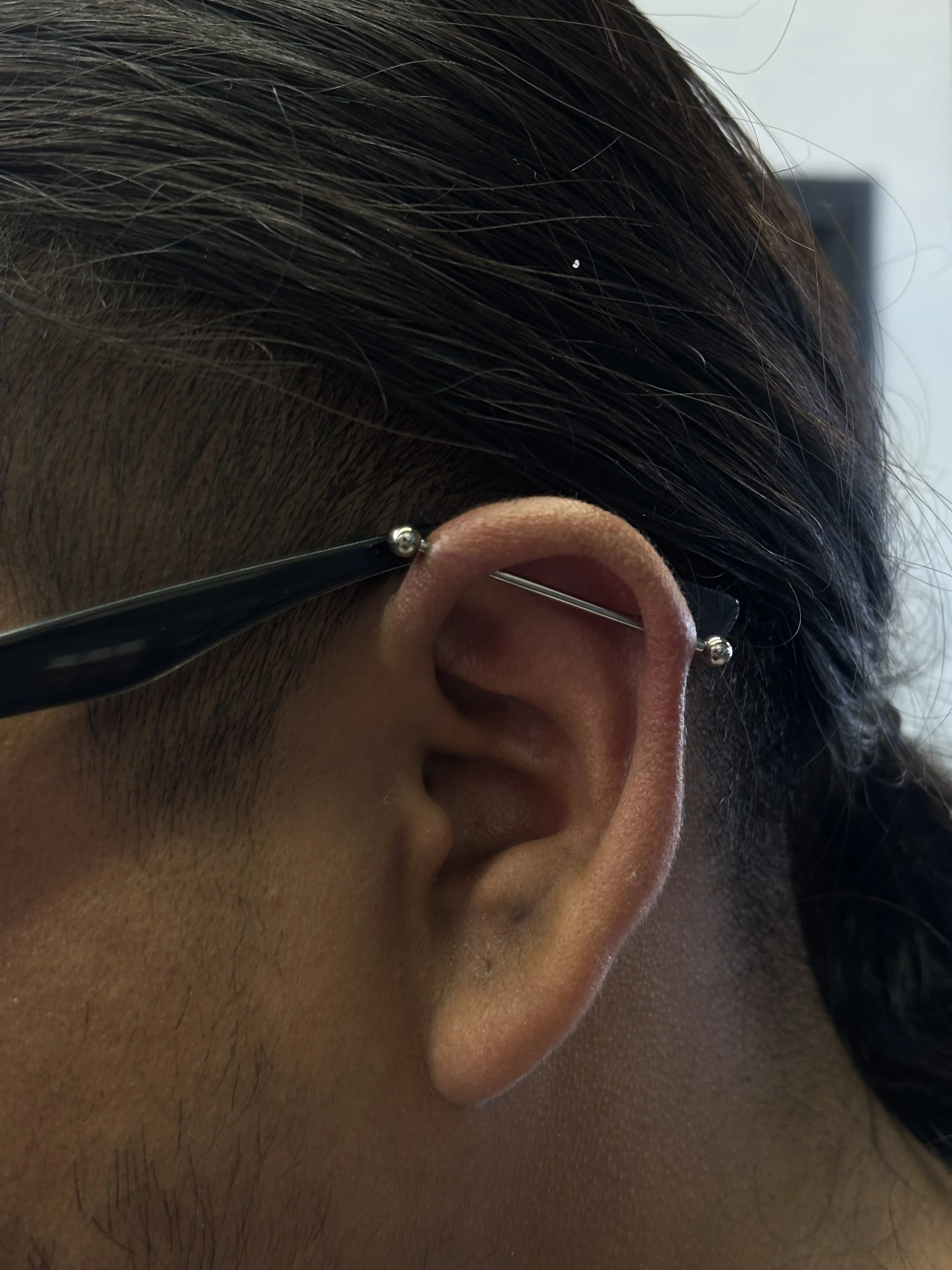 Close-up of a person's ear with a safety pin inserted through the upper part of the ear.