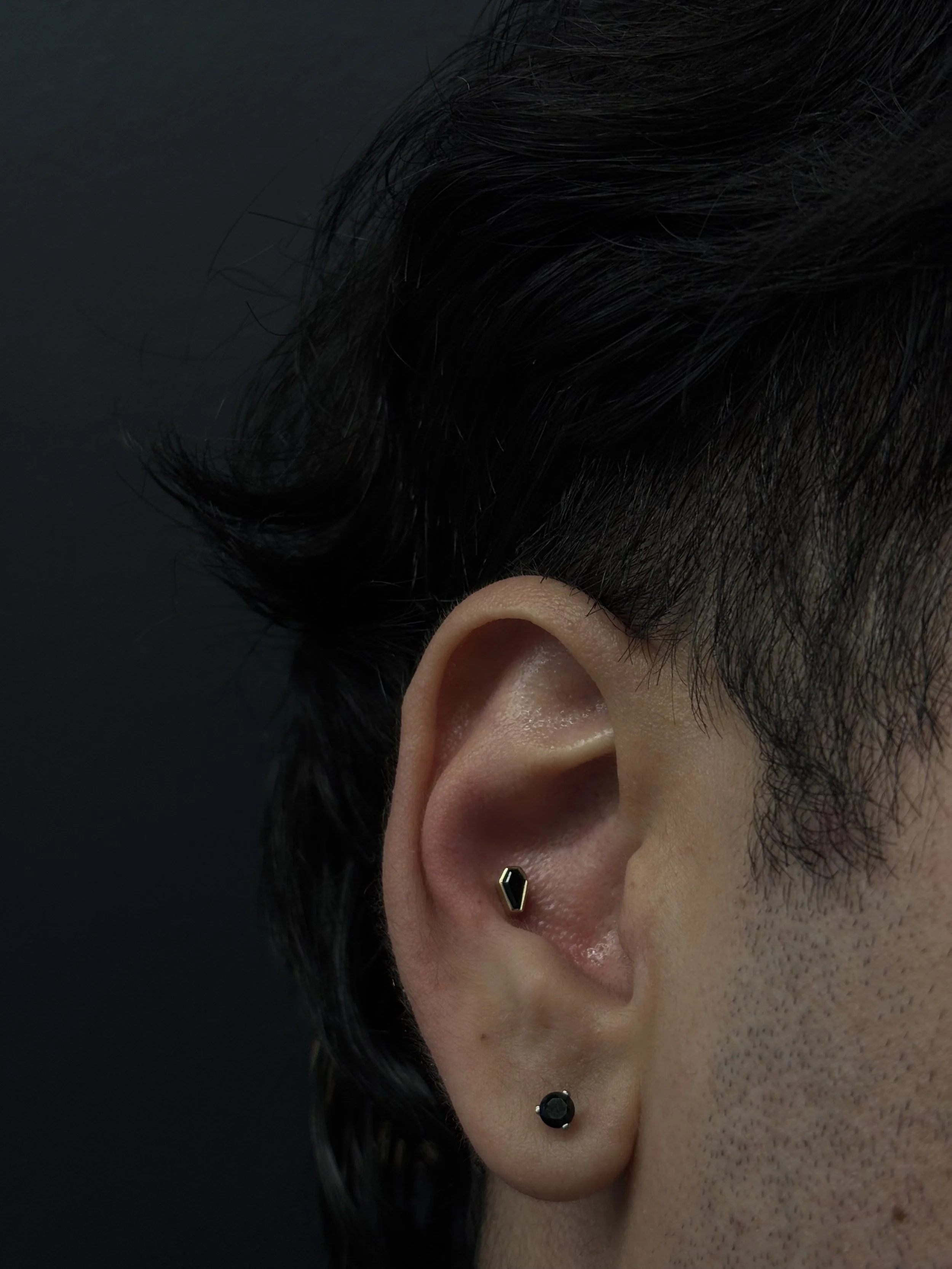 Close-up of a person's ear with black hair and a small black stud earring.