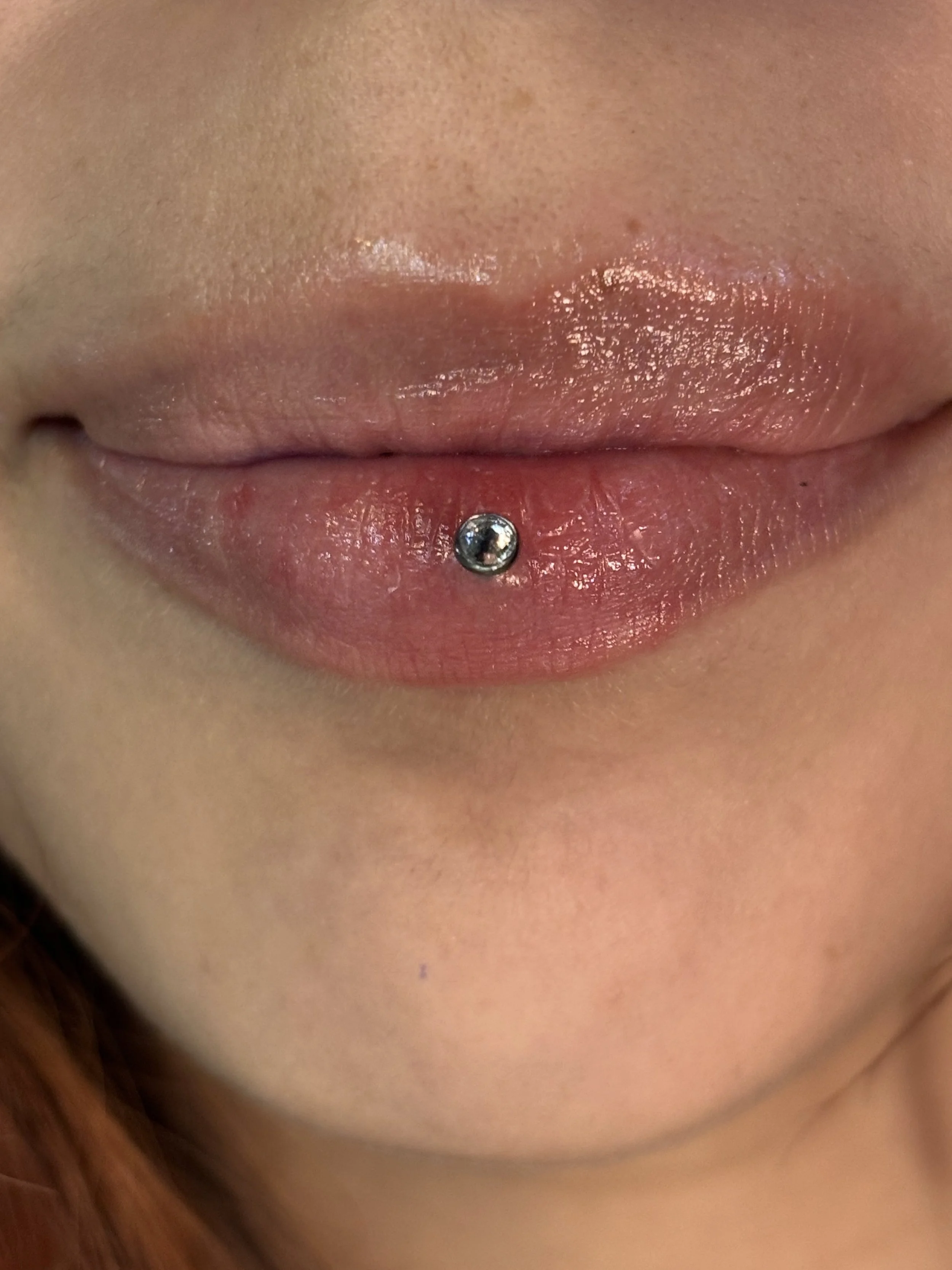 Close-up image of lips with a lip piercing and textured skin.