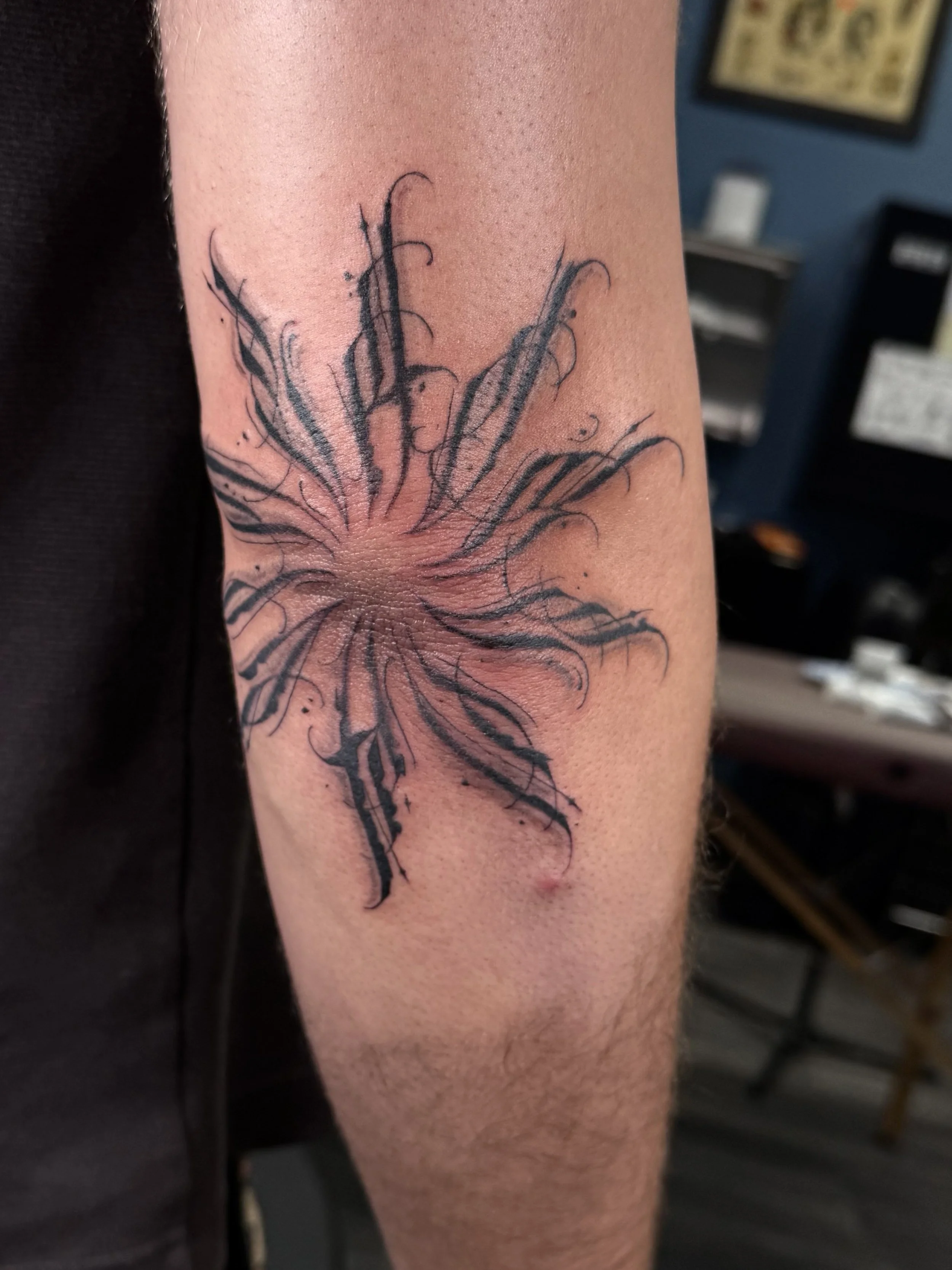 A tattoo of a detailed, black, and gray flower on a person's upper arm.