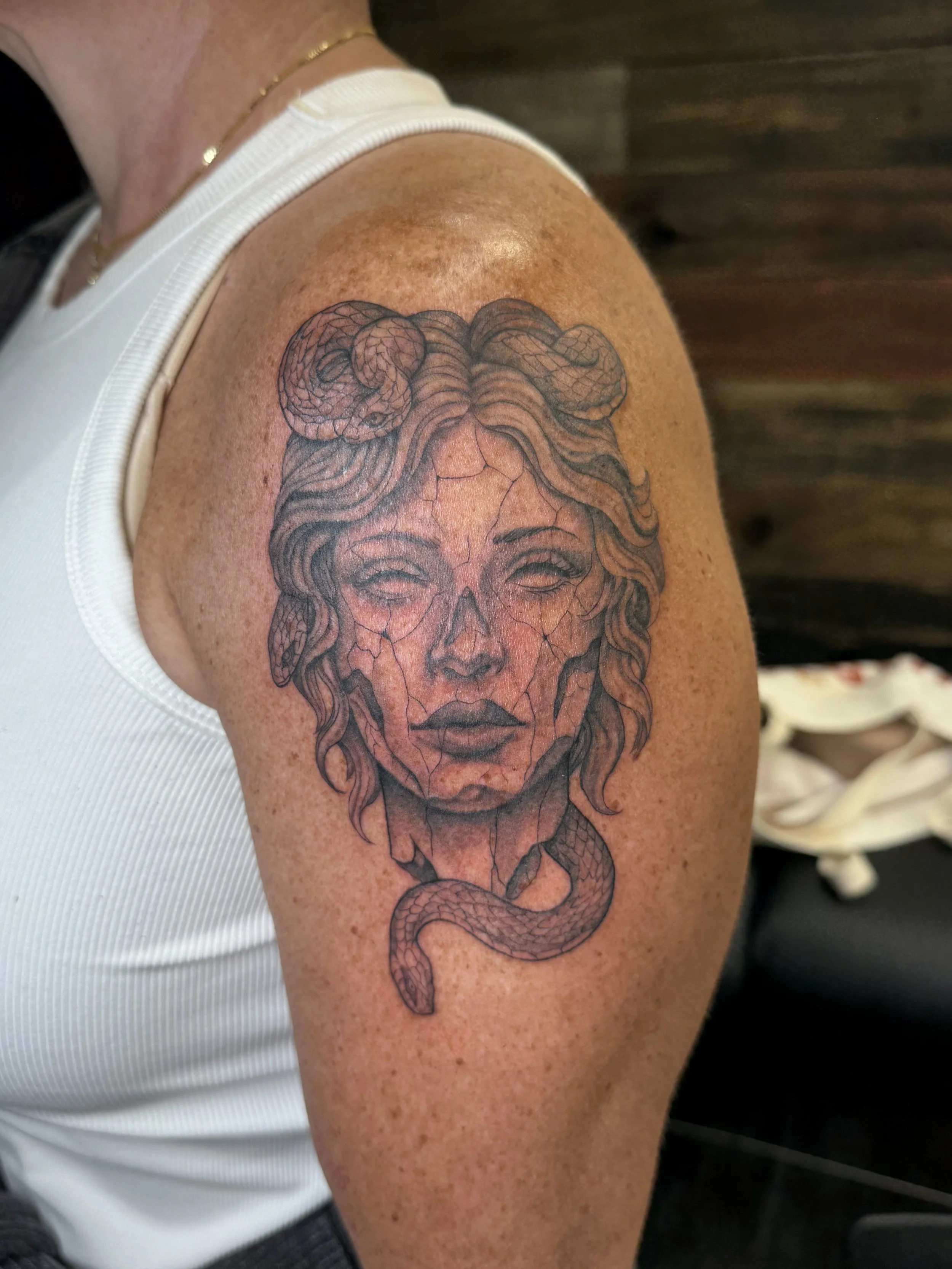 Tattoo of a woman's face with snake hair on upper arm, with detailed line work and shading.