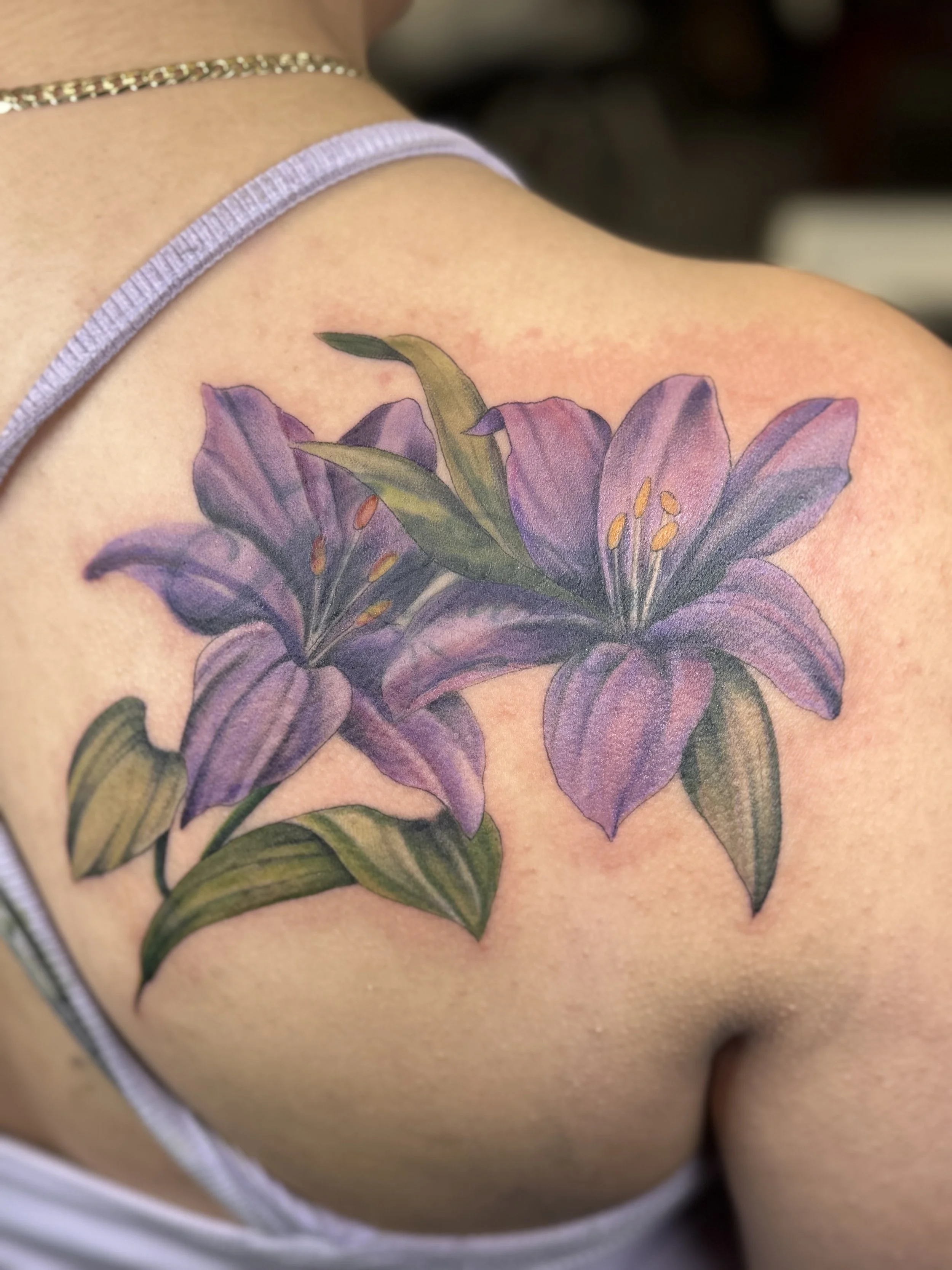 Close-up of a colorful lily tattoo on a person's shoulder.