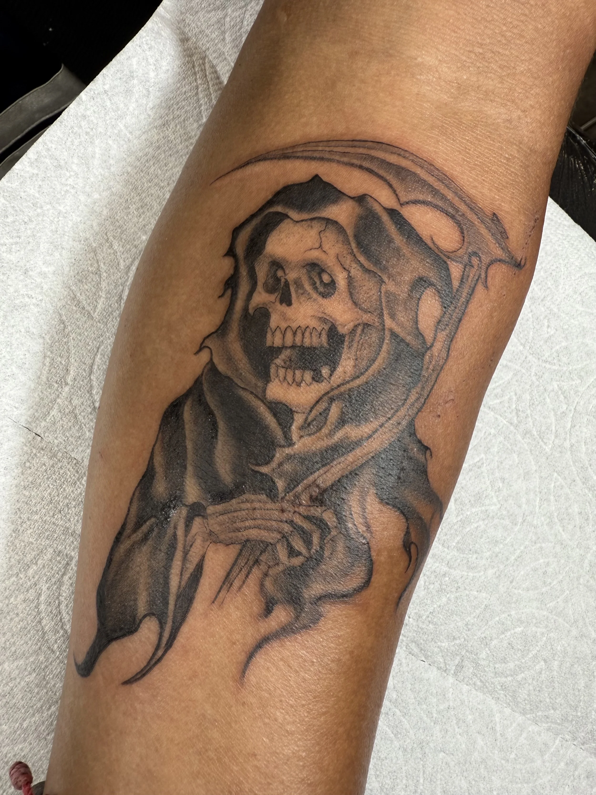 Tattoo of a human skull and a snake on a person's leg.
