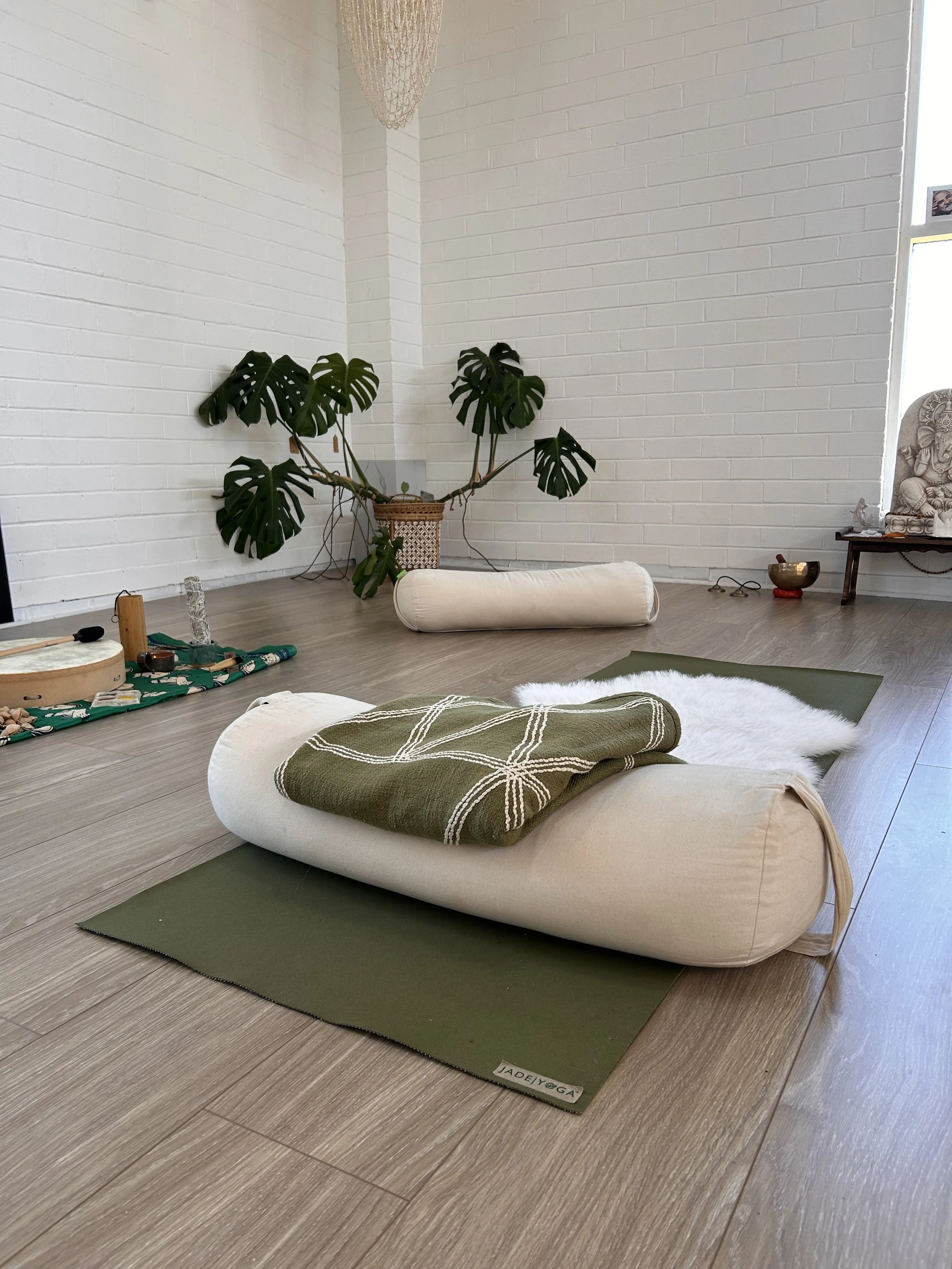 A quiet 1:1 breathwork session space with floor cushions, a bolster, and a monster plant against a brick wall.