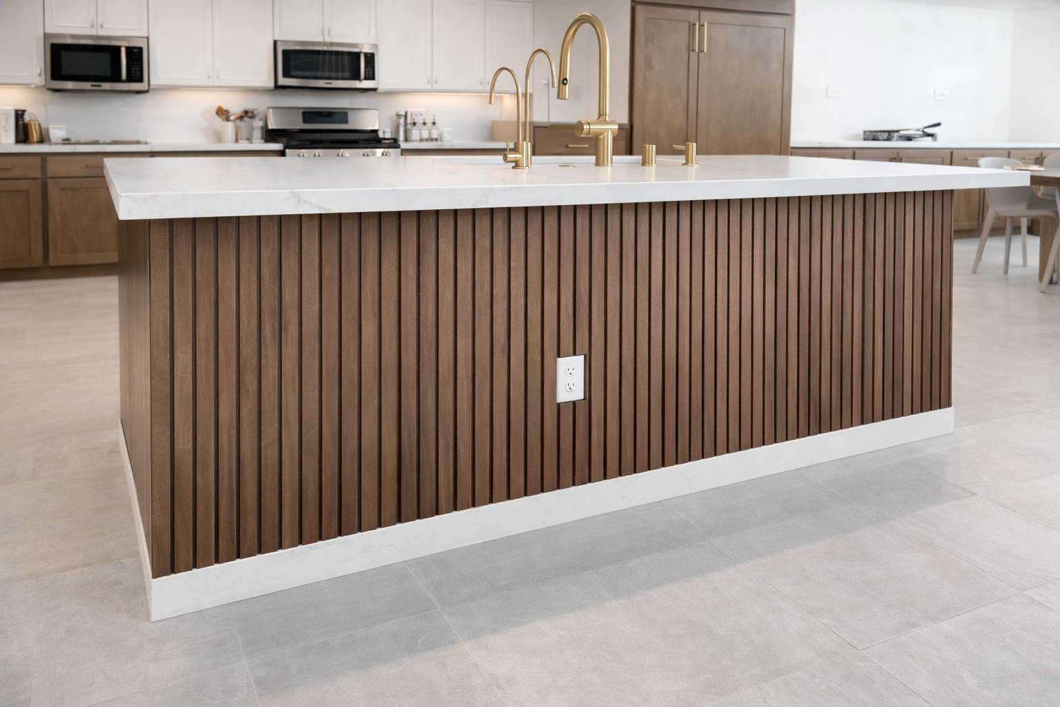 Modern kitchen island with white marble countertop, brass faucet, and brown wooden paneling, in a spacious kitchen with built-in appliances and light-colored flooring.