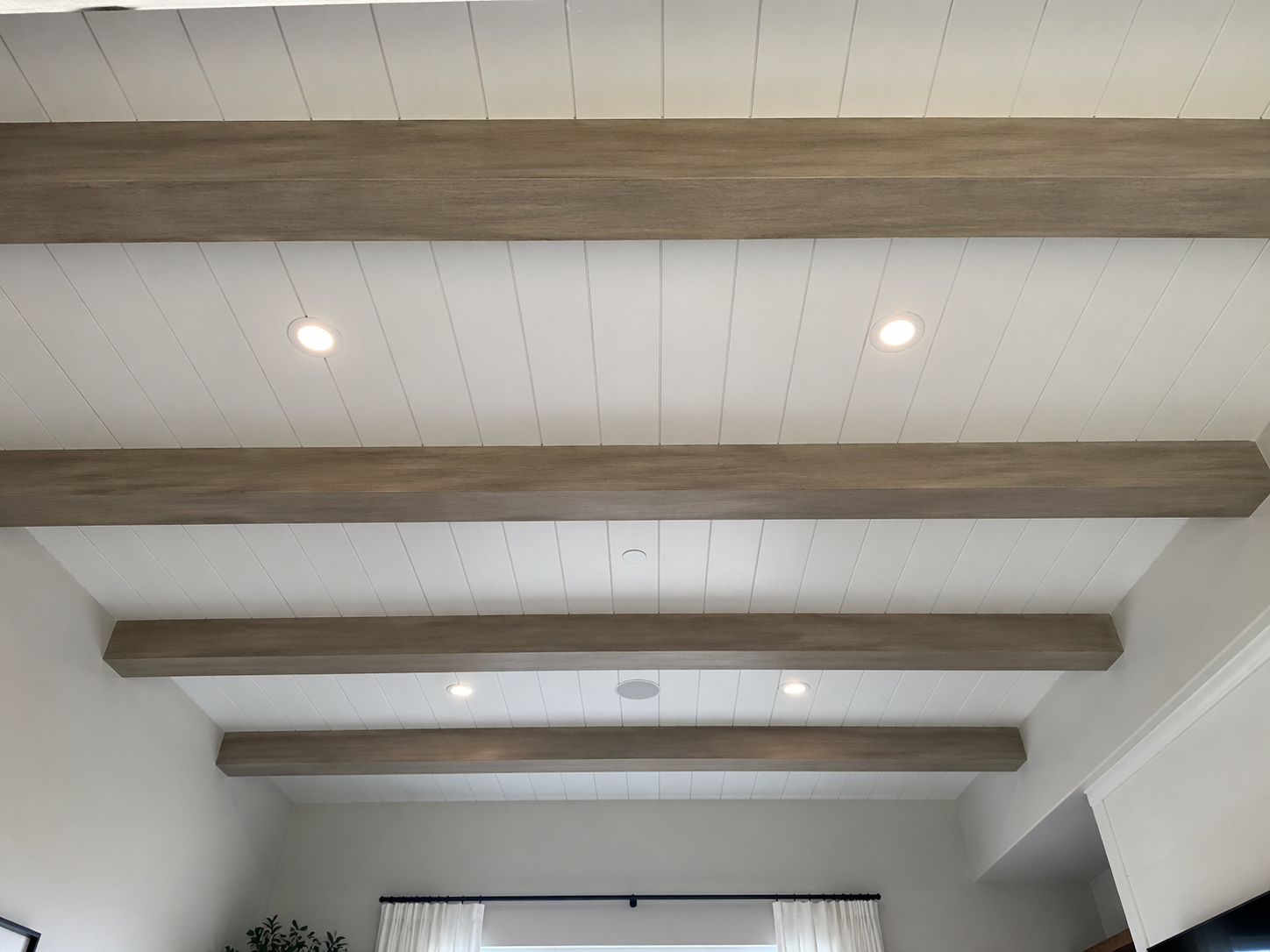 Ceiling with white wooden panels and four evenly spaced wooden beams, each with recessed lighting.