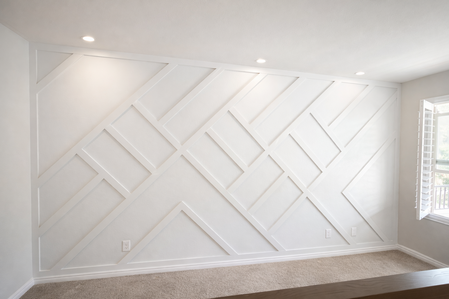 Empty white wall with geometric wood trim pattern, three ceiling lights, window with shutters, and beige carpet.