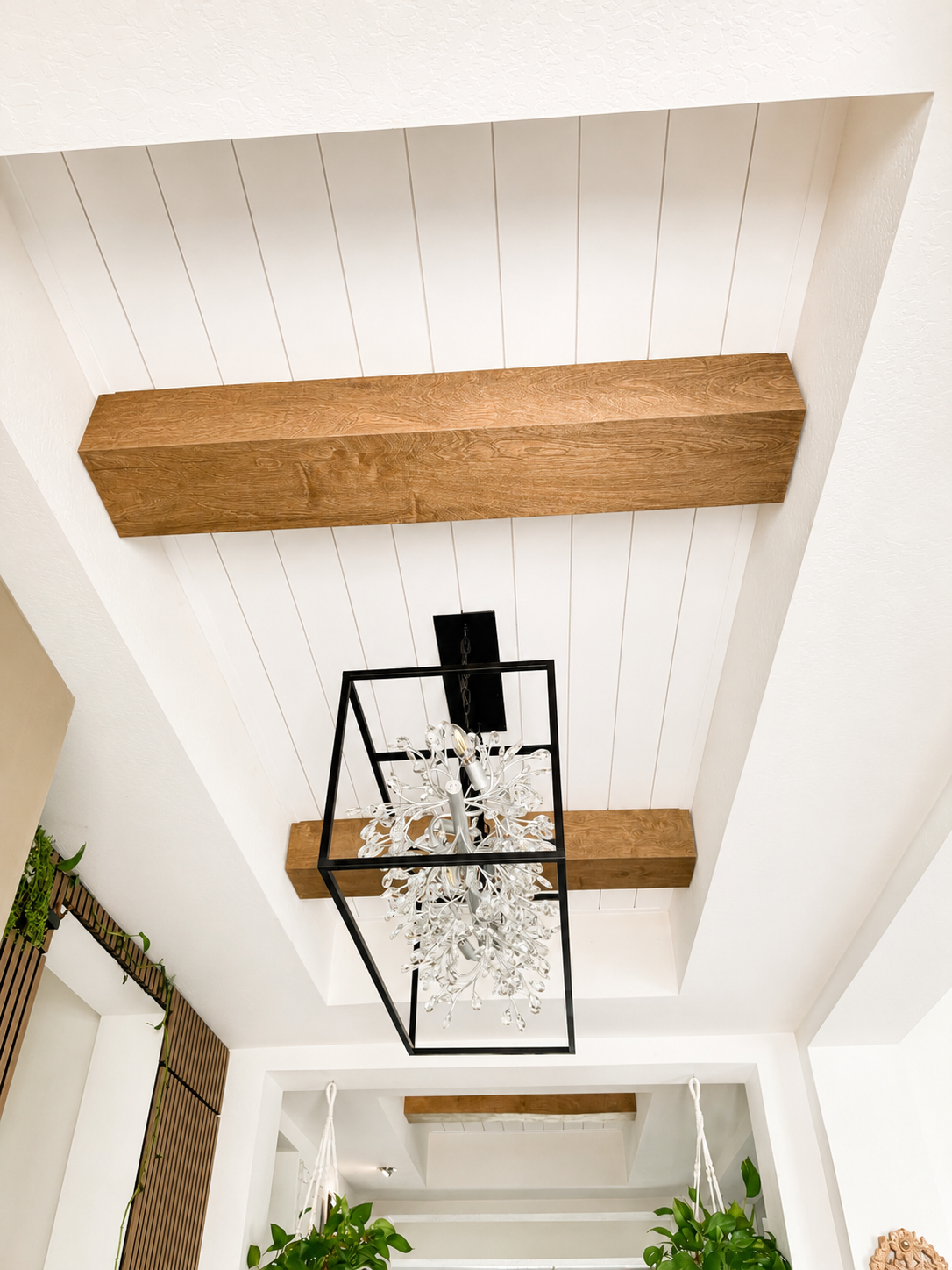 Ceiling with two wooden beams, a hanging chandelier, and white paneled ceiling.