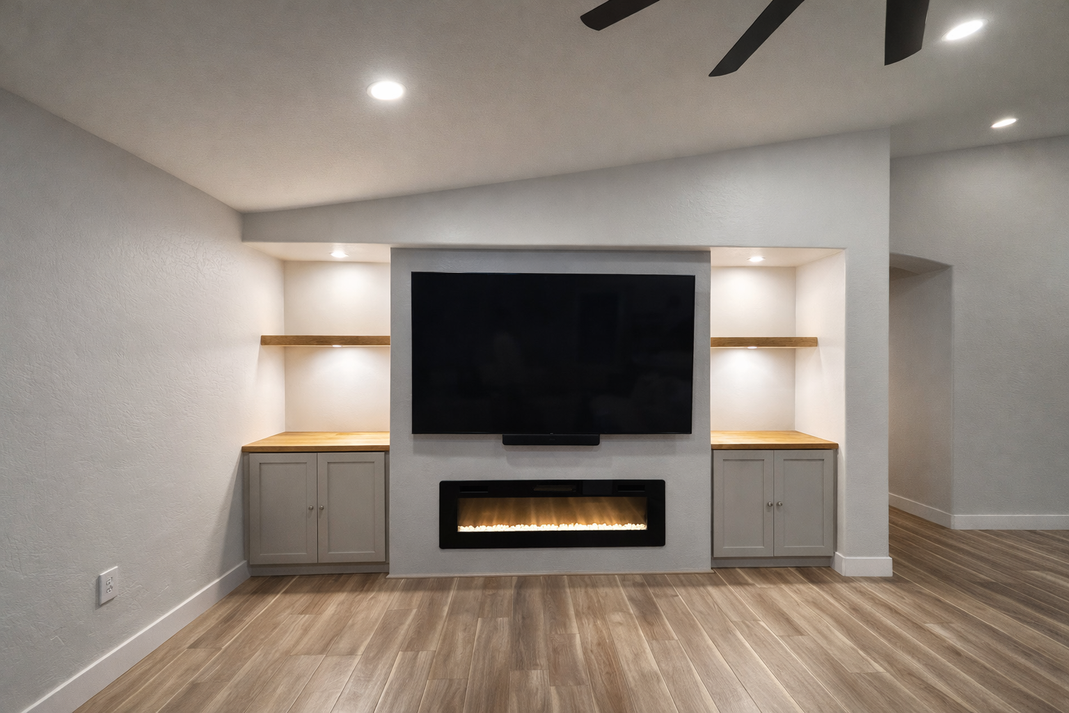 Living room with wall-mounted TV above an electric fireplace, built-in shelving units on each side, and wood flooring.