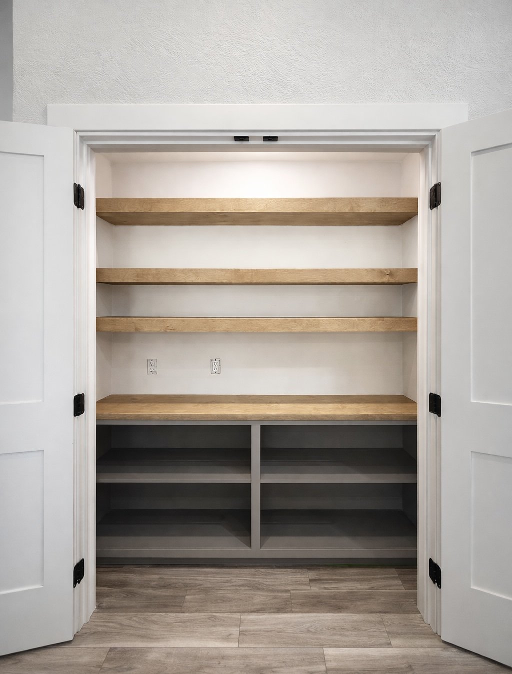 Empty built-in closet with three wooden shelves and gray lower shelves, white walls, and open white double doors.
