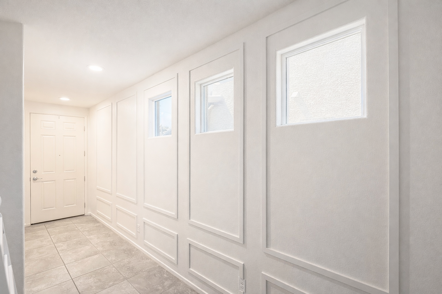 Bright hallway with white walls, three small windows, and gray tiled flooring.