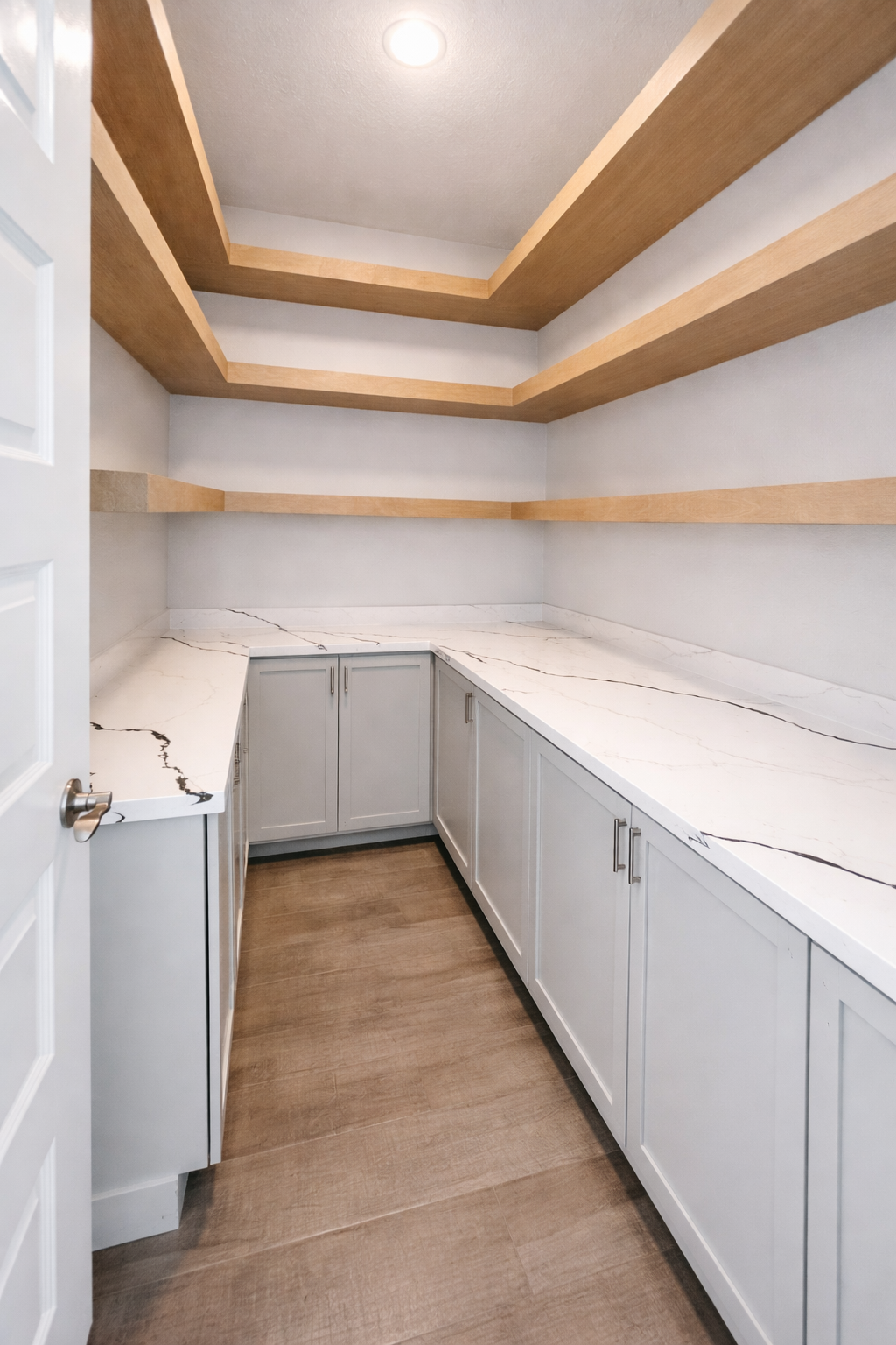 Empty walk-in pantry with white cabinets, marble countertops, and wooden shelves.