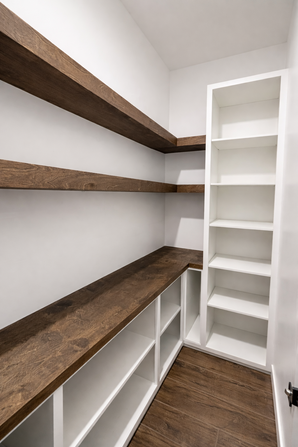Empty walk-in closet with white walls, brown wooden shelves, and a white bookcase.