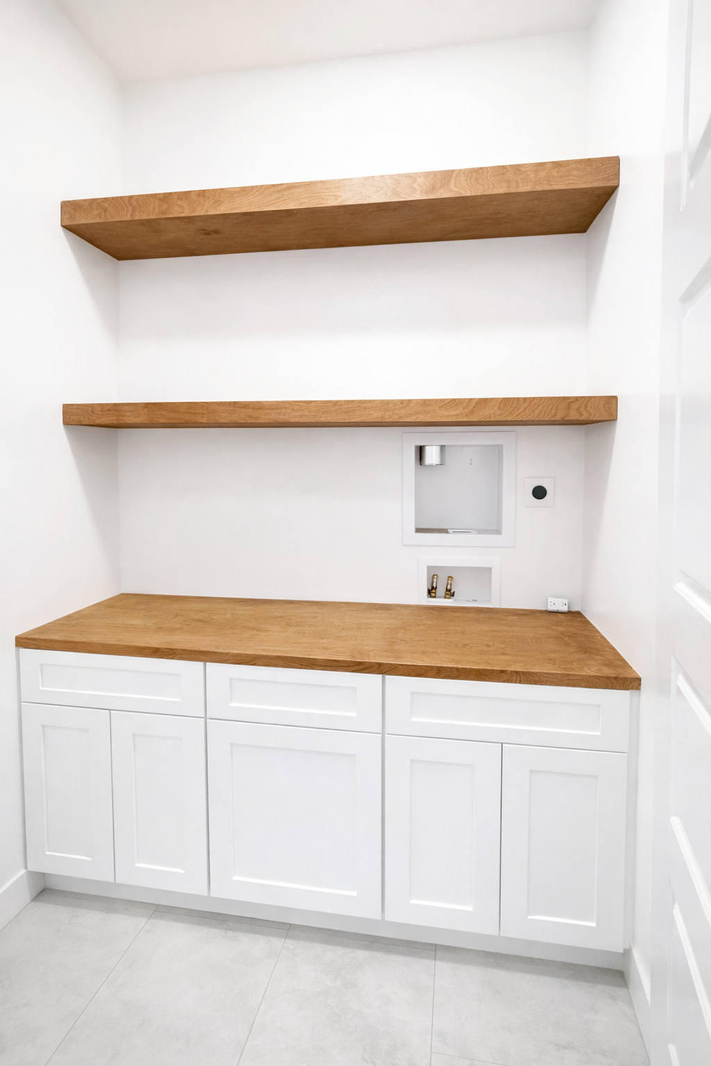 Empty laundry room with white cabinets, wooden countertop, and floating wooden shelves on white walls.