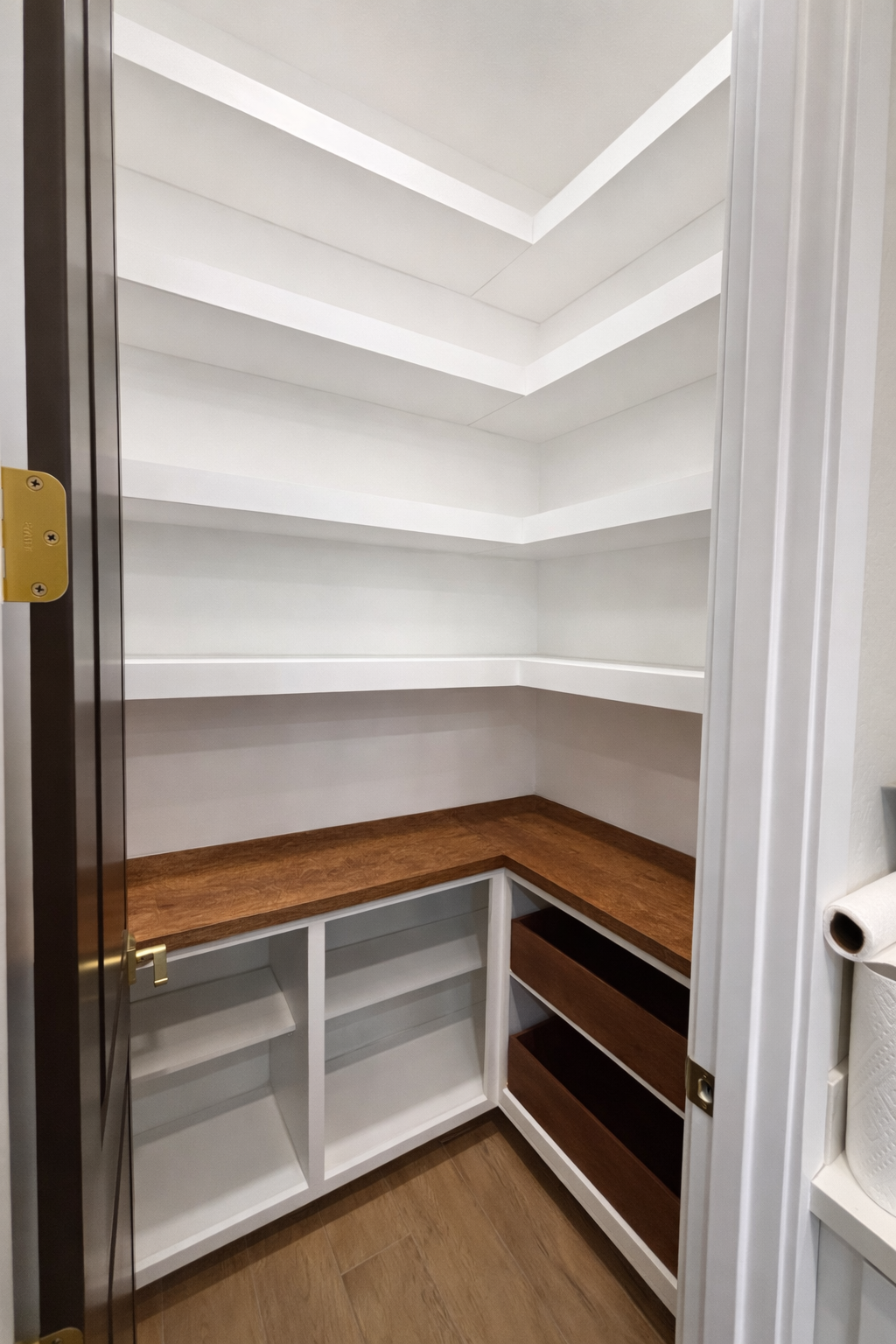 Empty white pantry with wooden shelves and countertop, next to a roll of paper towels.