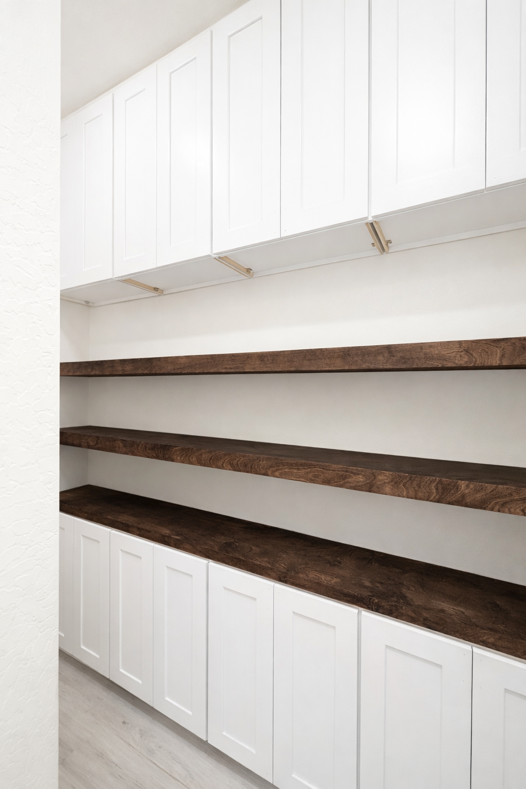 Empty kitchen pantry with white cabinets and dark wooden shelves.