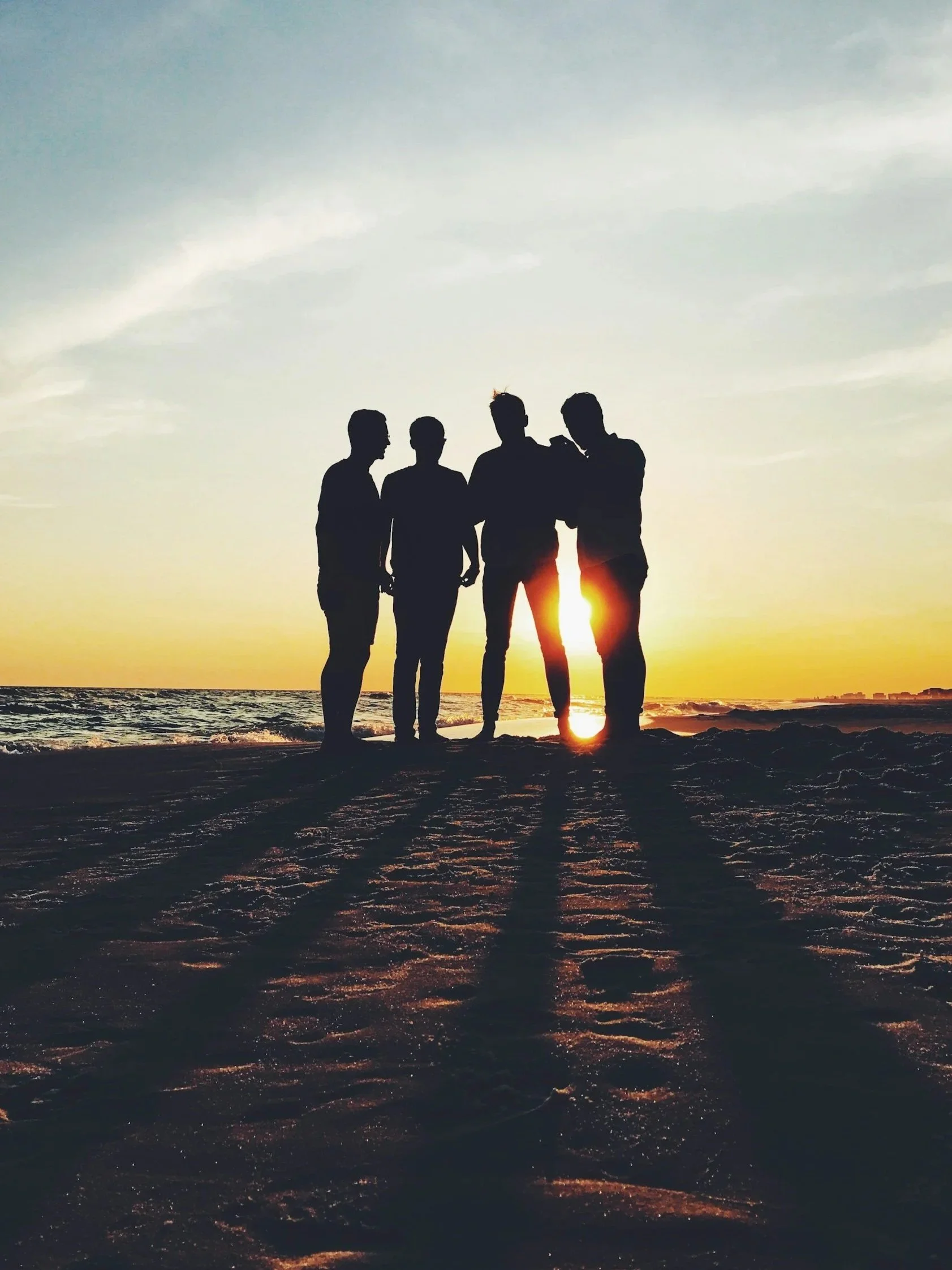 Haven, young adults group.

Silhouetted group of four people standing on a beach at sunset with the ocean in the background.