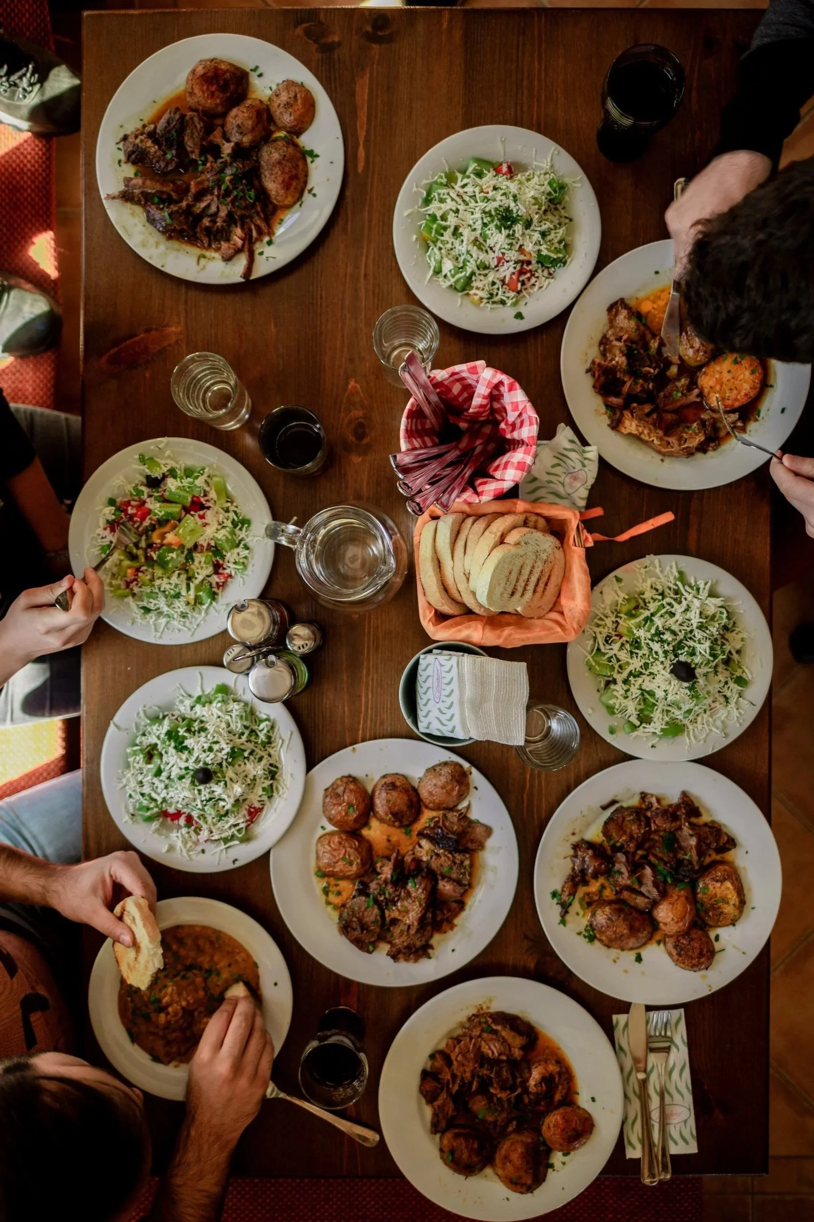 Community Groups picture, eating together.

A top-down view of a wooden dining table set with plates of salads, roasted meat, bread, and drinks, with hands reaching for food.