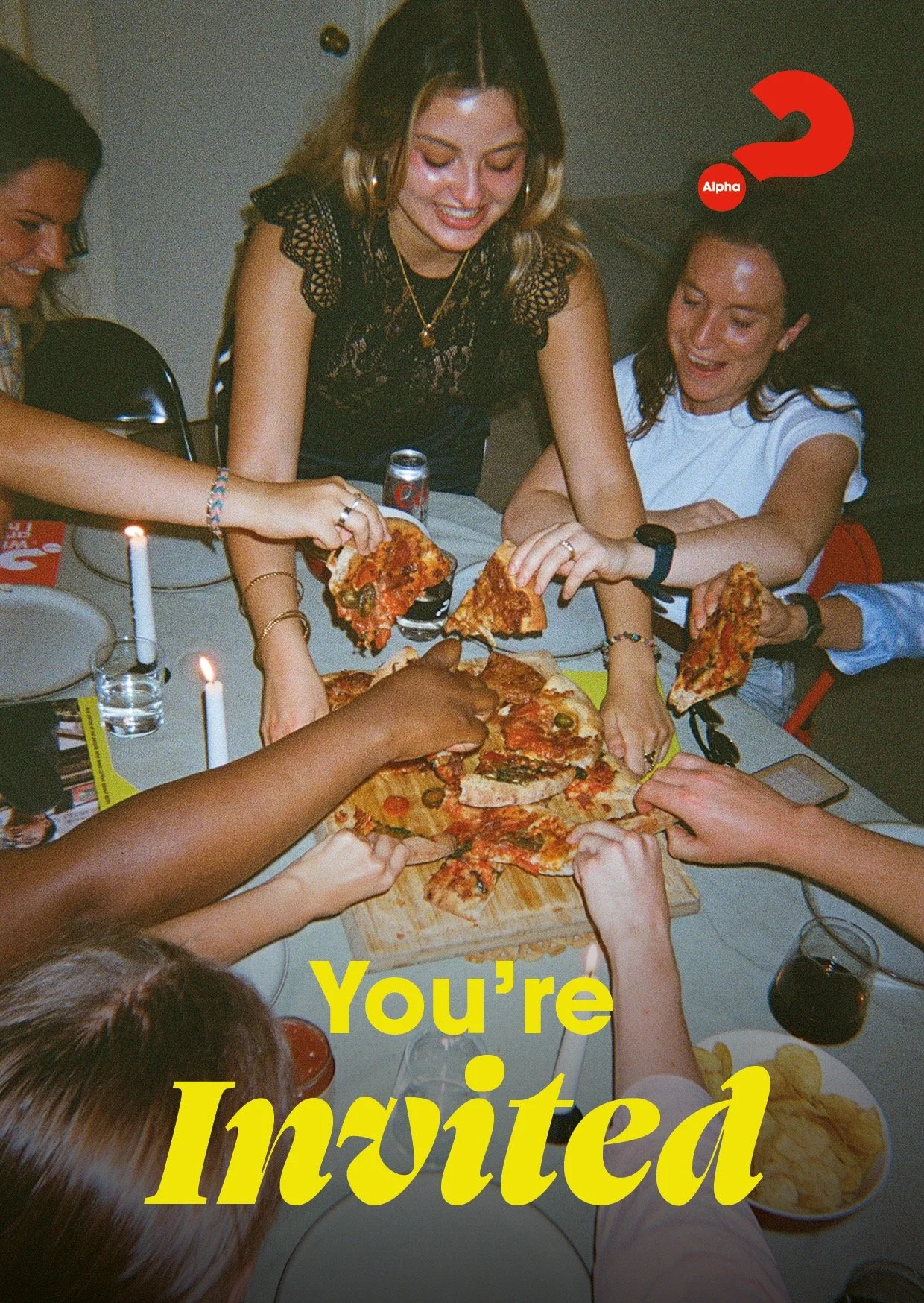 Group of people gathered around a table eating pizza, with candles and drinks, celebrating and enjoying a social gathering.
