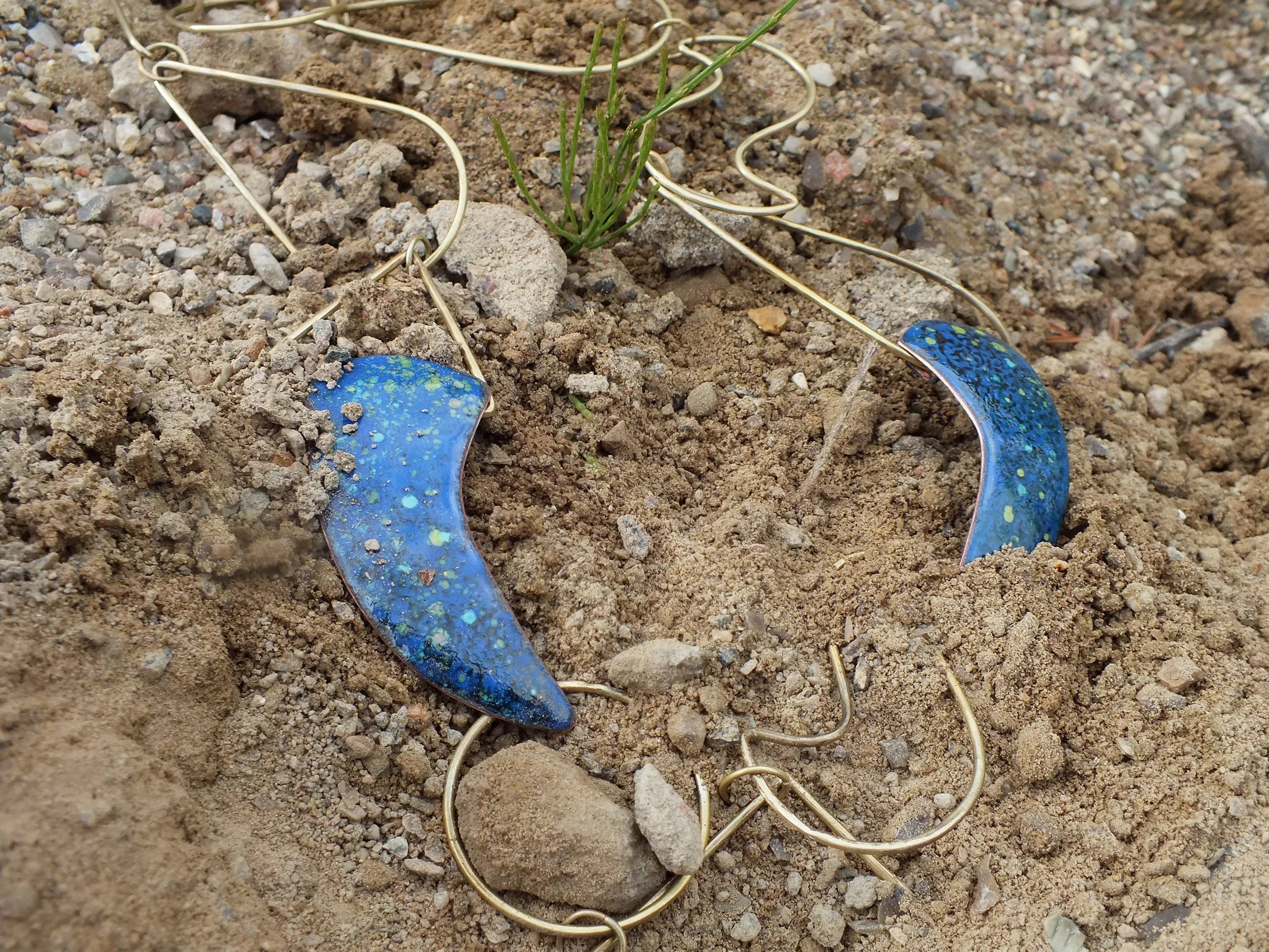 Eine Kette aus Messingelementen und Kupfer-Emaille, angelehnt an die minoische Kunst, liegt wie ein ärchaologisches Artefakt vergraben im Boden.