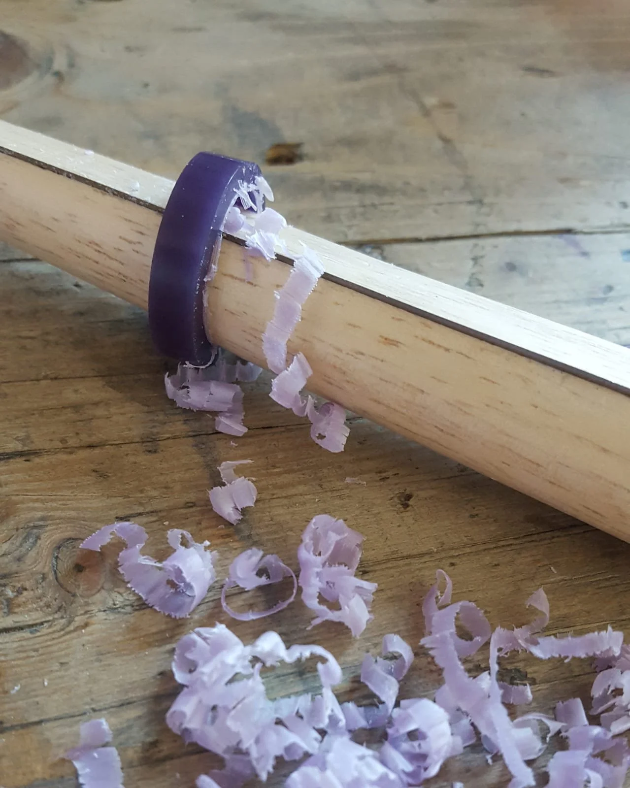 Ein Wachsrohling mit Wachsspähnen der Bearbeitung und nach oben gerichtete Holzspäne auf einer Holzunterlage.