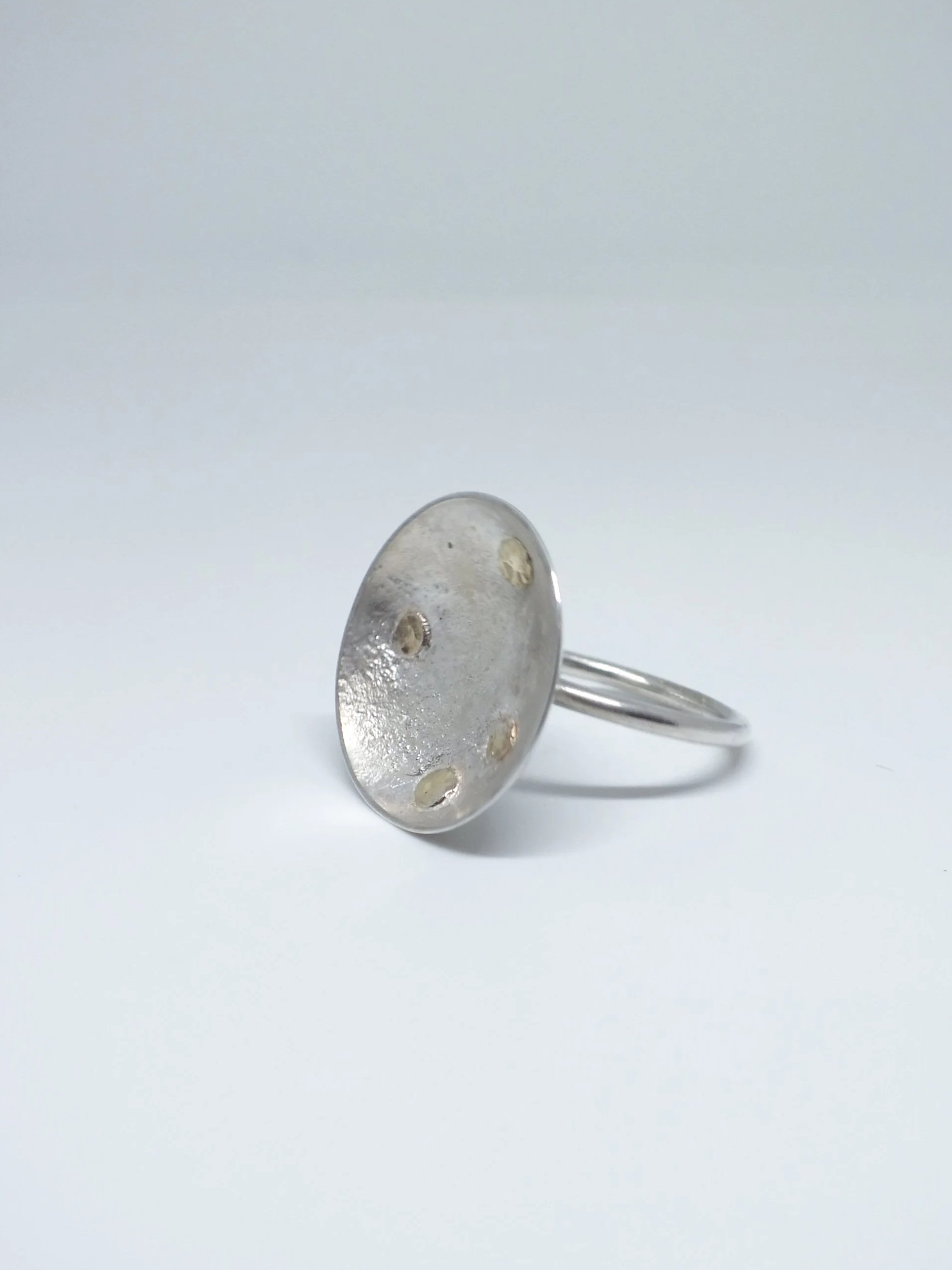 Silberner Ring im Schalendesign mit goldenen Nieten, sieht aus wie ein Sternenhimmel, auf weißem Hintergrund.