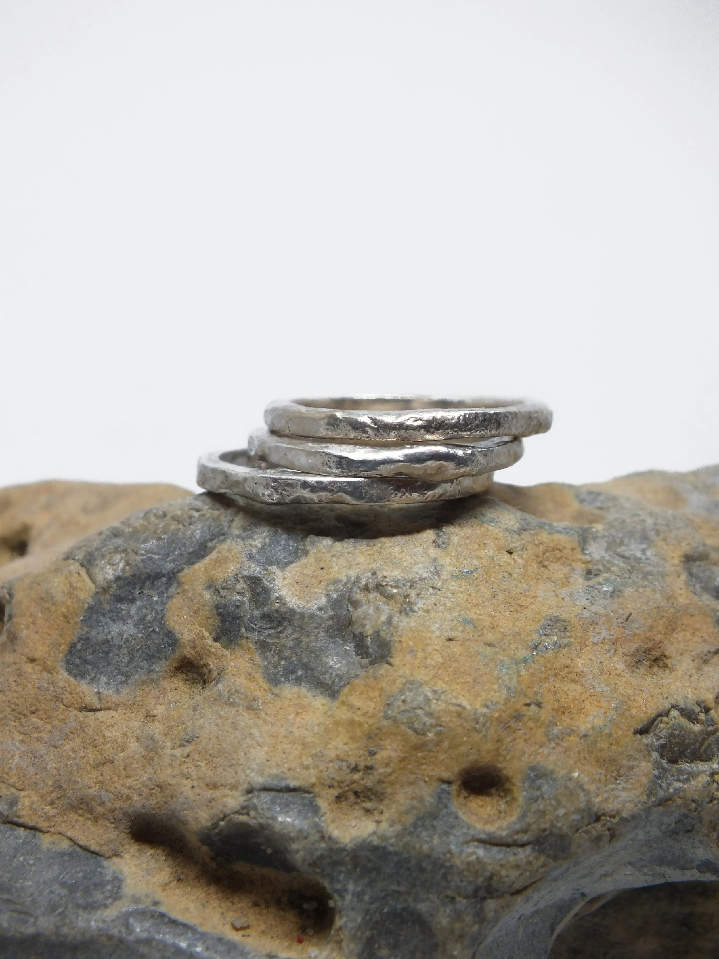 Eine Reihe von silbernen Ringen, gestapelt auf einem Stein, vor einem weißen Hintergrund.