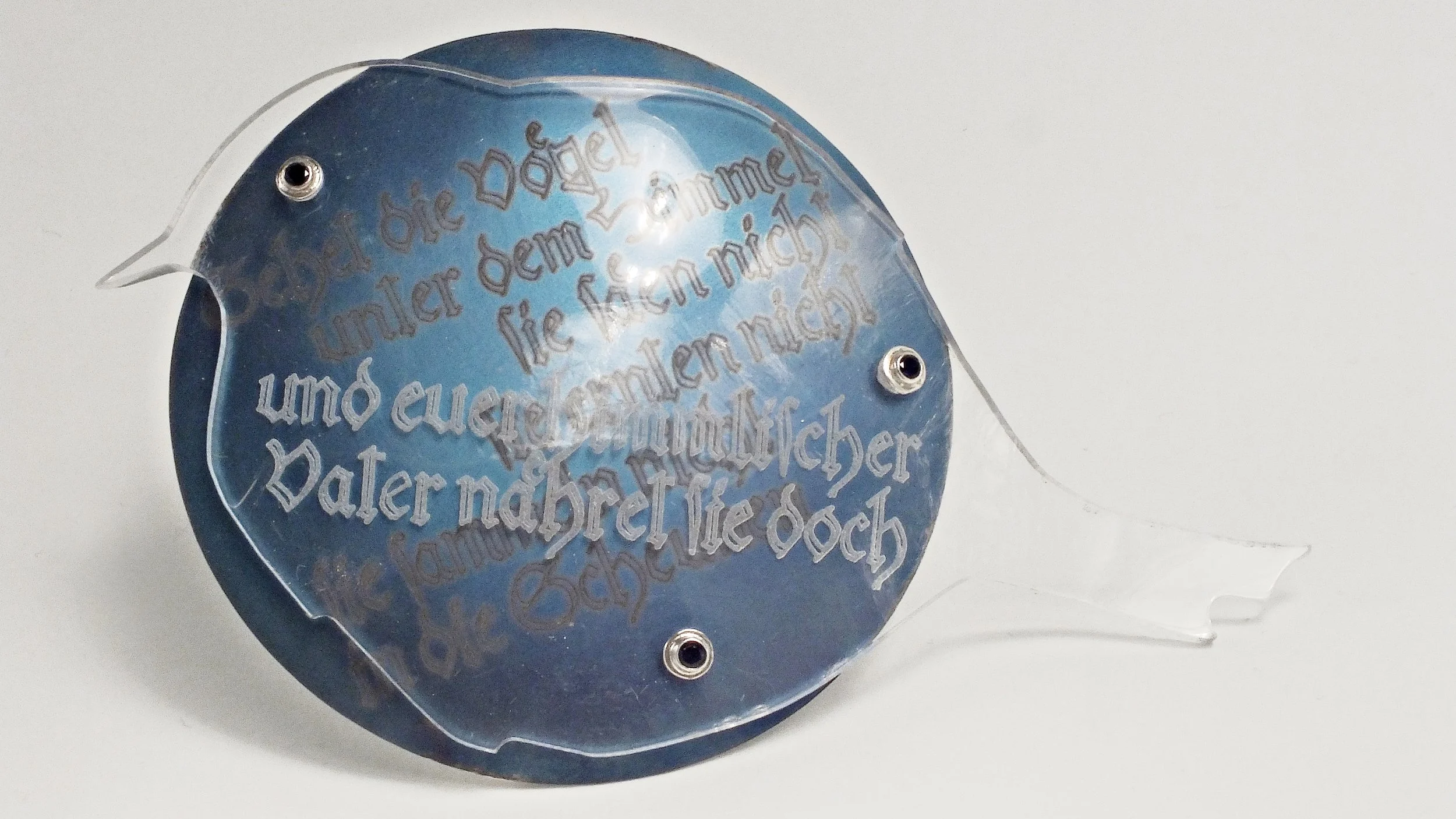 Eine silberne Schalenbrosche, auf der passend zu einer der biblischen Losung: Sehet die Vögel im Himmel, ein Vogel aus Plexiglas montiert ist.