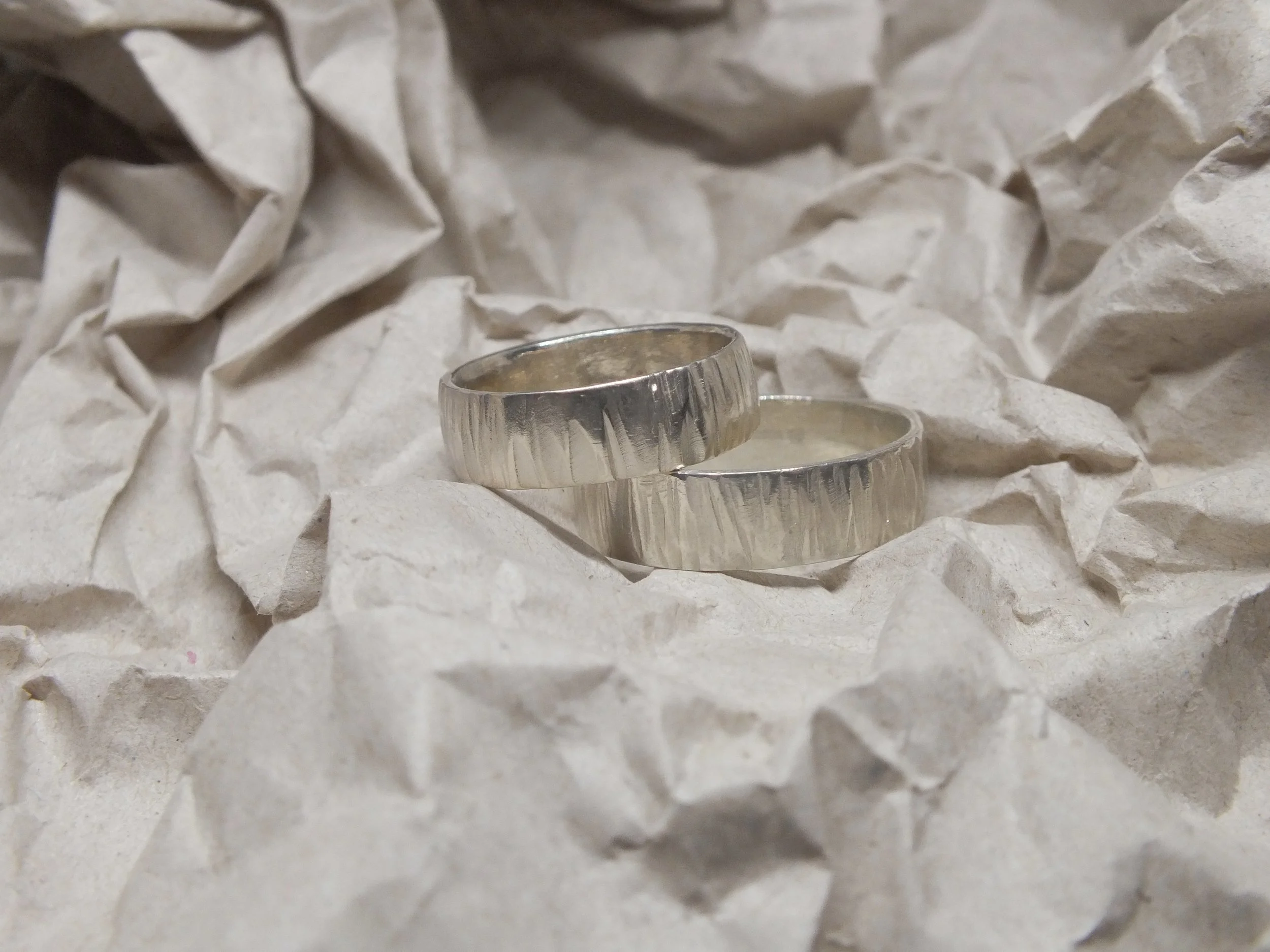 Zwei silberne Ringe auf zerknülltem weißen Papier.