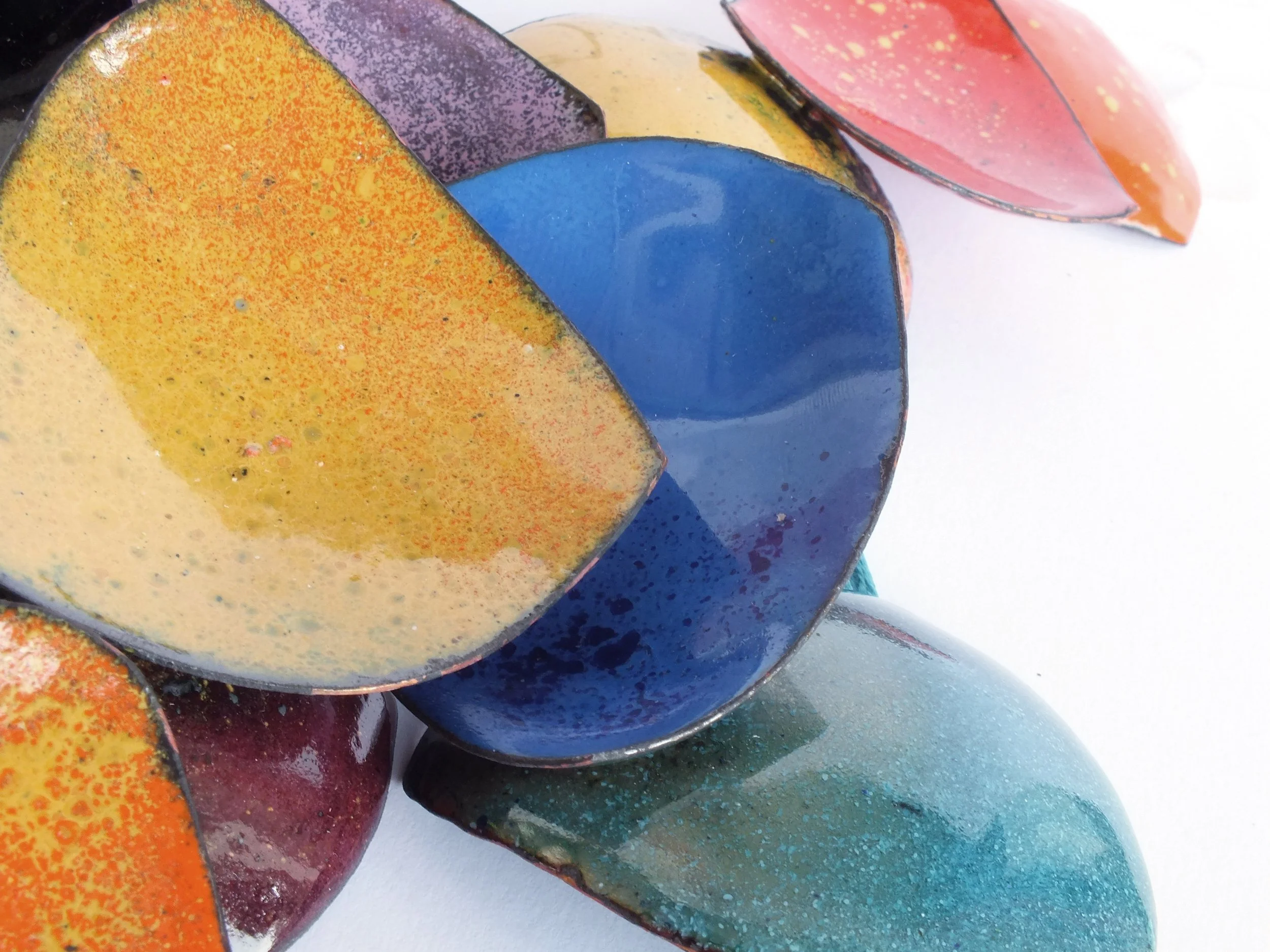 Bunte Emaille-Schalen übereinandergestapelt, in Farben wie gelb, blau, rot, grün und lila, mit unterschiedlichen Oberflächenstrukturen, Ausschnitt eines Kettenanhängers.